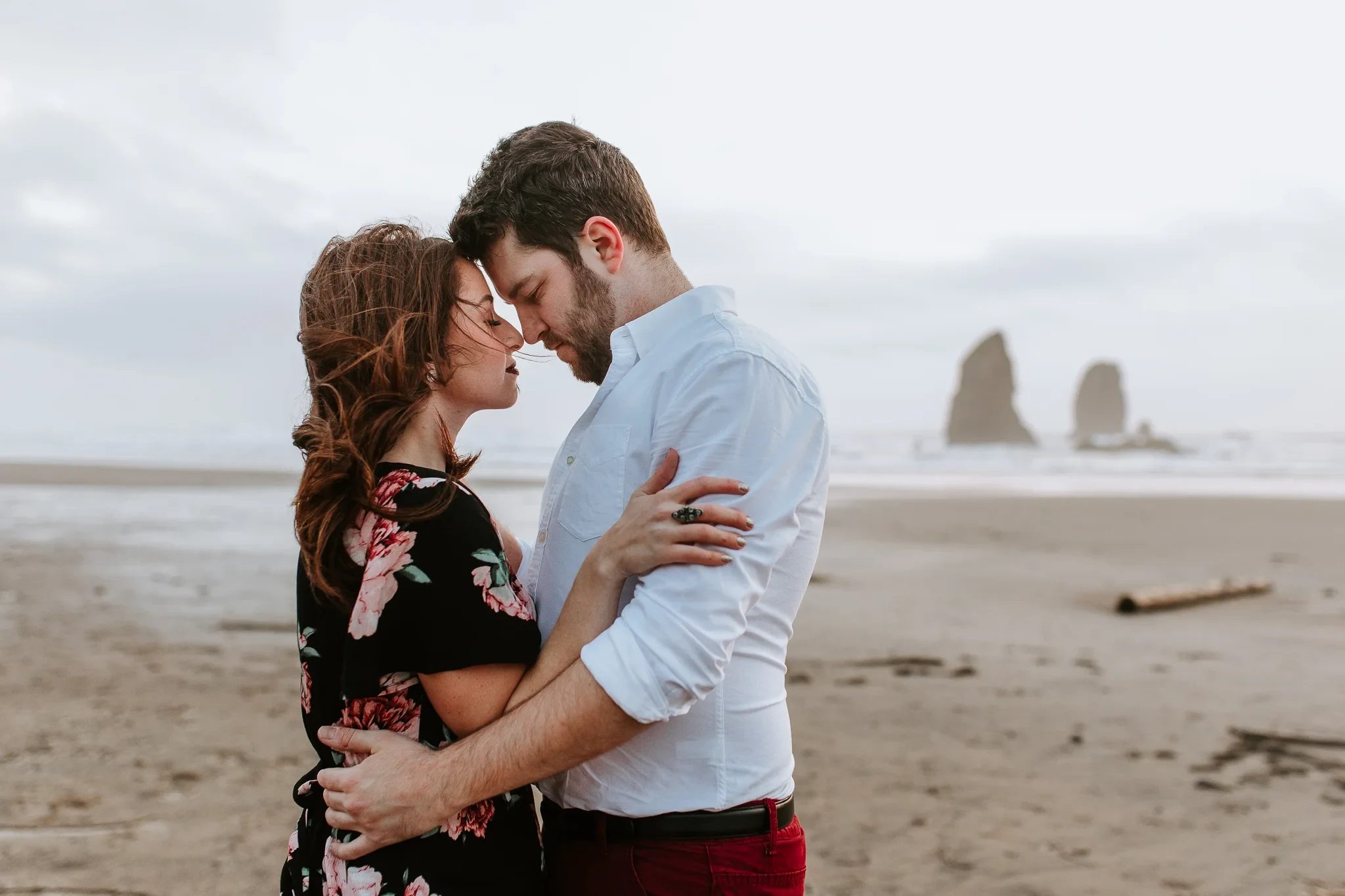 Two adults touch foreheads with waves and sea stacks behind them