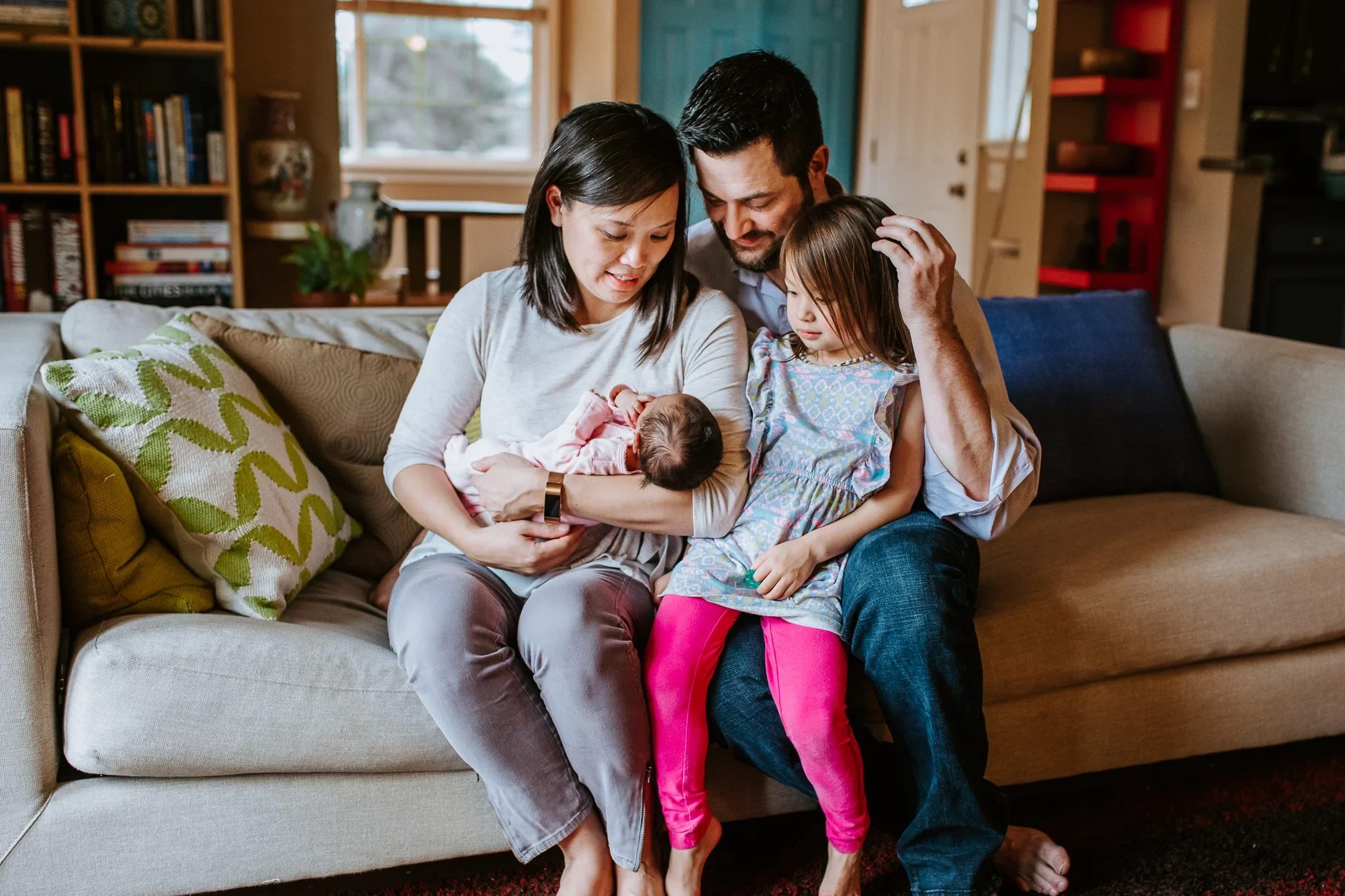 Two adults and a child gather around a baby on a sofa
