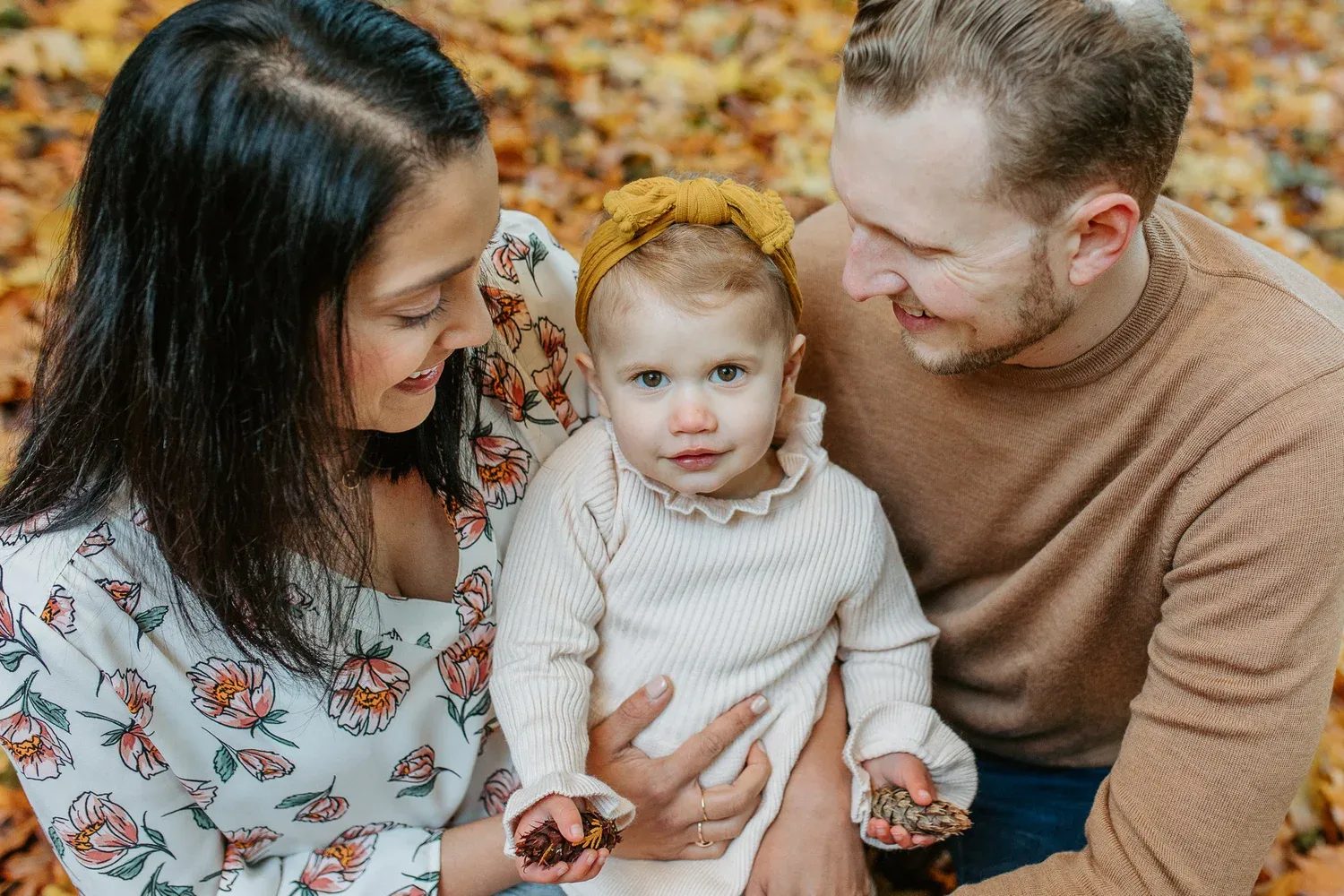 Two adults smile down at a toddler with a yellow bow