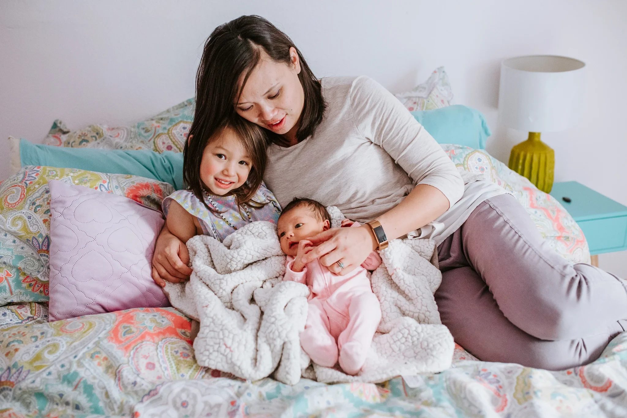 Woman and child lie beside a baby on a colorful bed