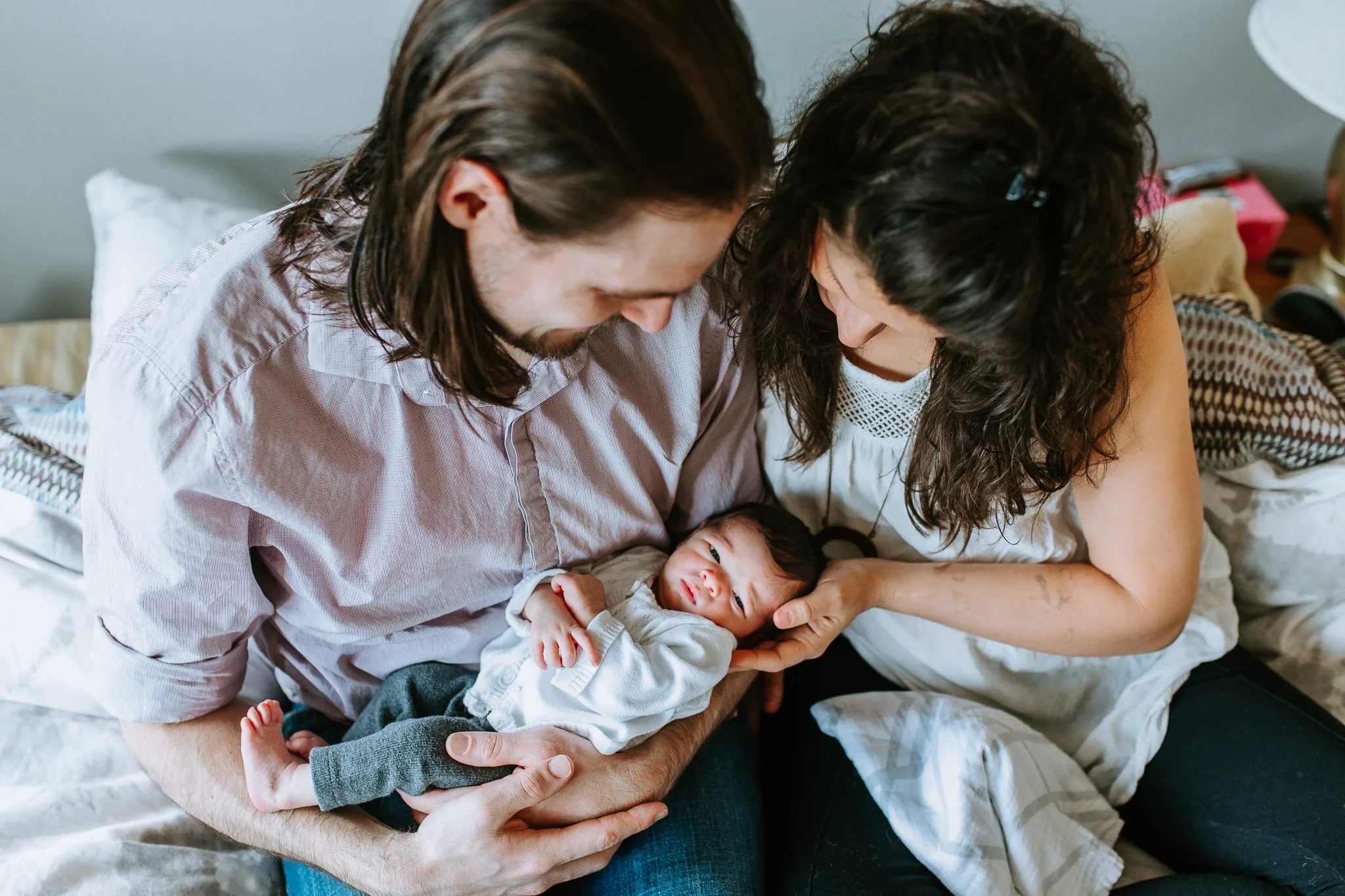 Two adults lean their heads together above the baby they are holding