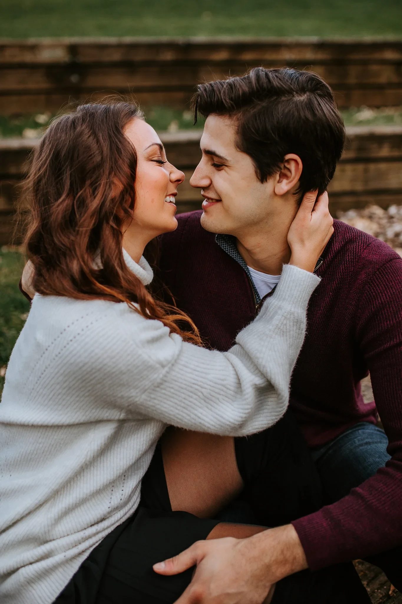Two adults smile nose to nose while seated on a park bench