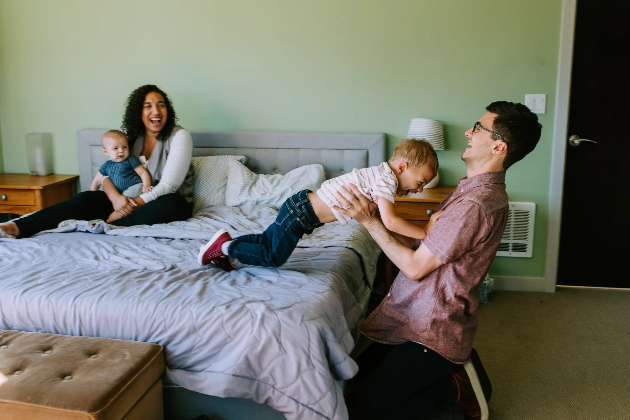 Family spreads out playfully across a bed and chair