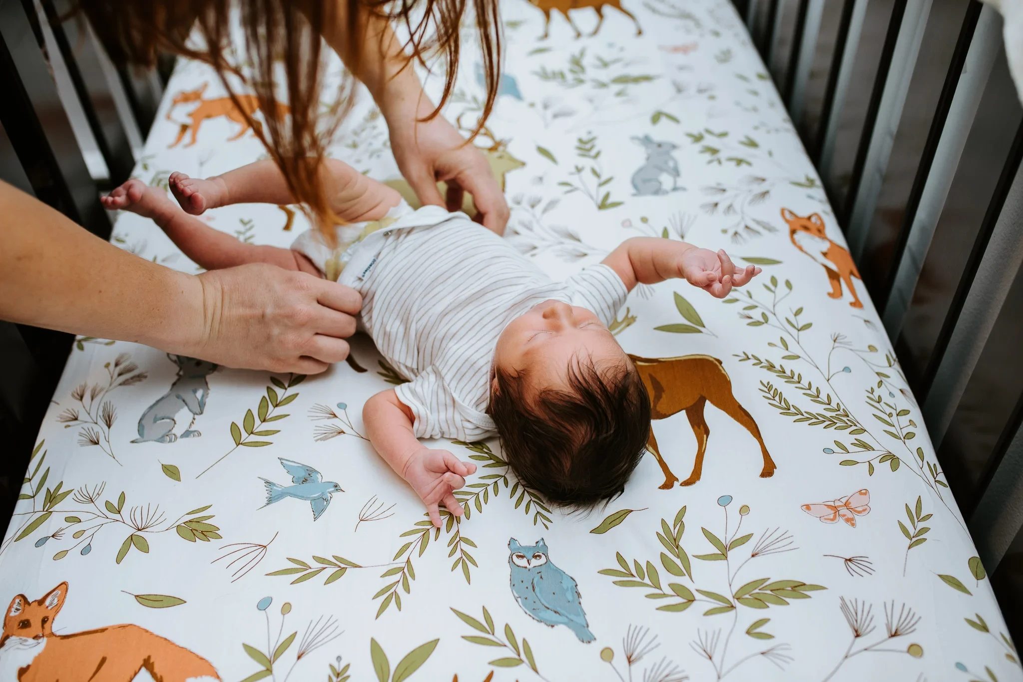 Hands gently settle a baby on a botanical-print changing pad
