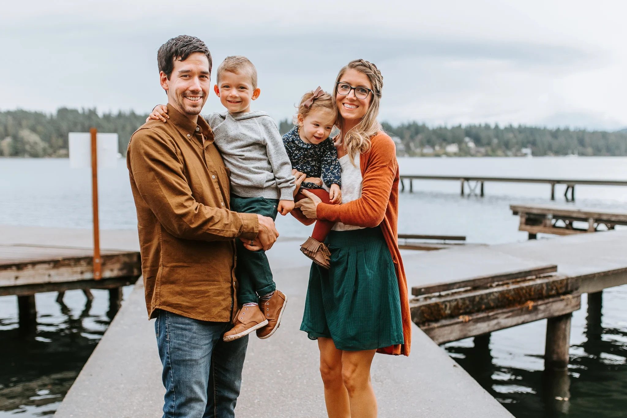 Four people stand together on a wooden dock beside a lake