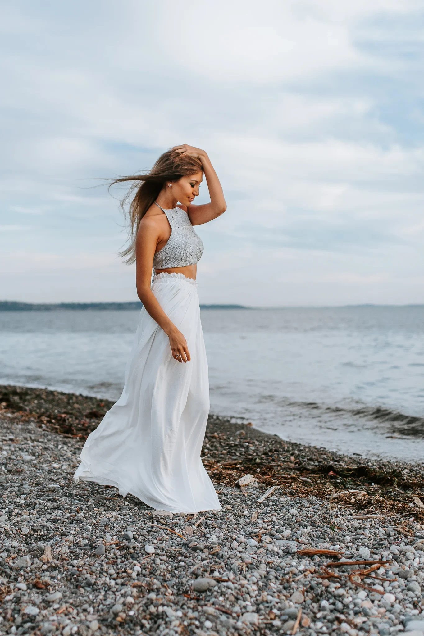Woman in a flowing white dress stands on a pebbled beach