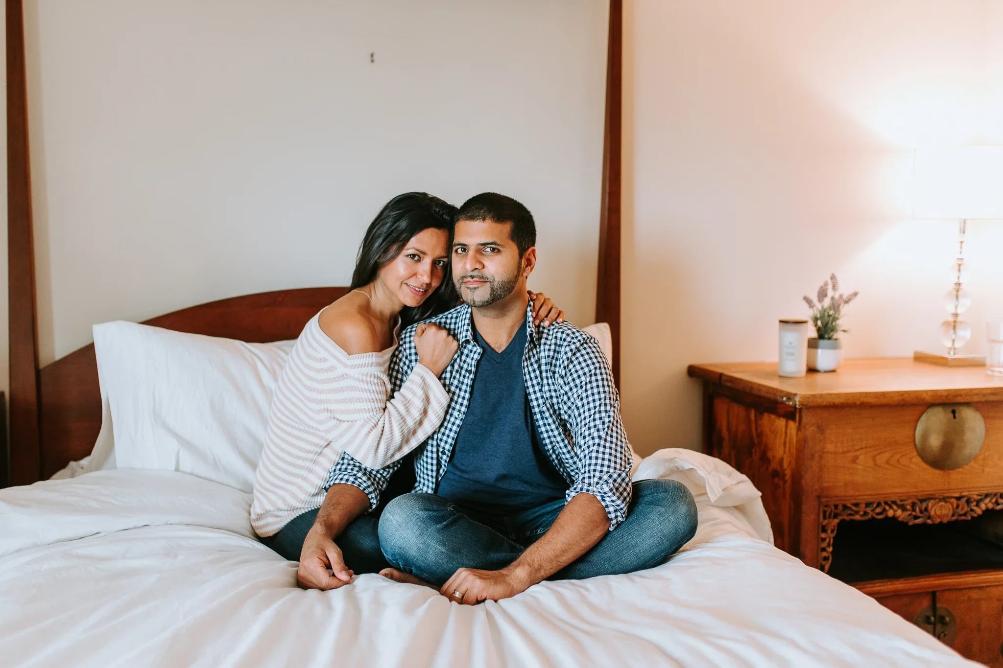 Two adults sit close together on a four-poster bed