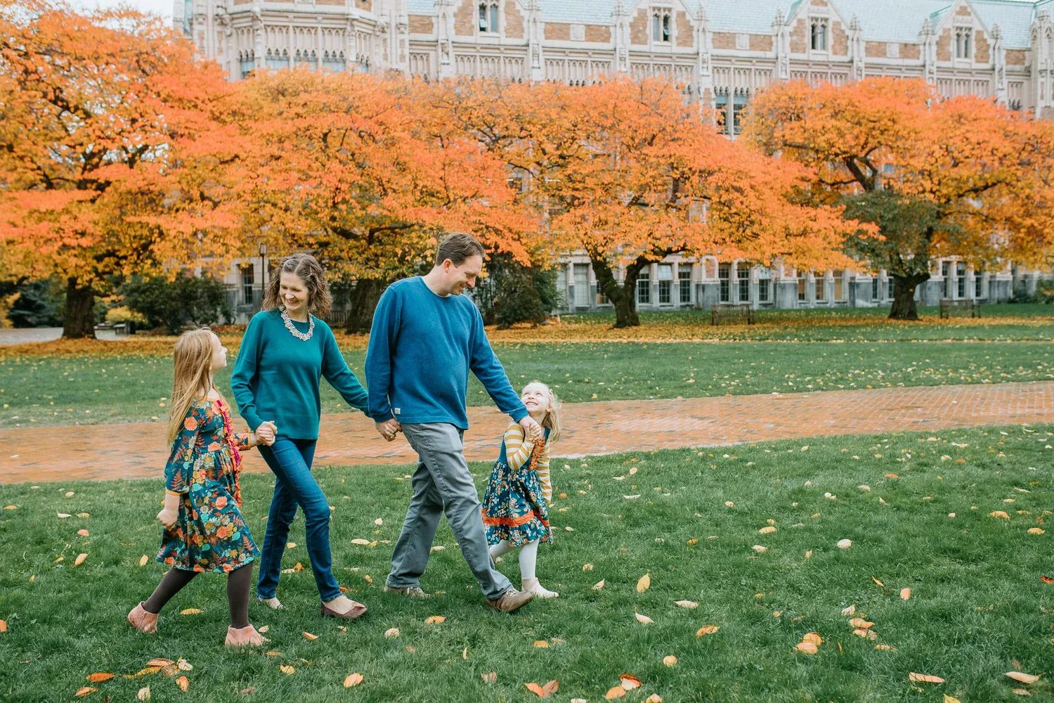 Family walks across a lawn beneath vivid orange autumn trees
