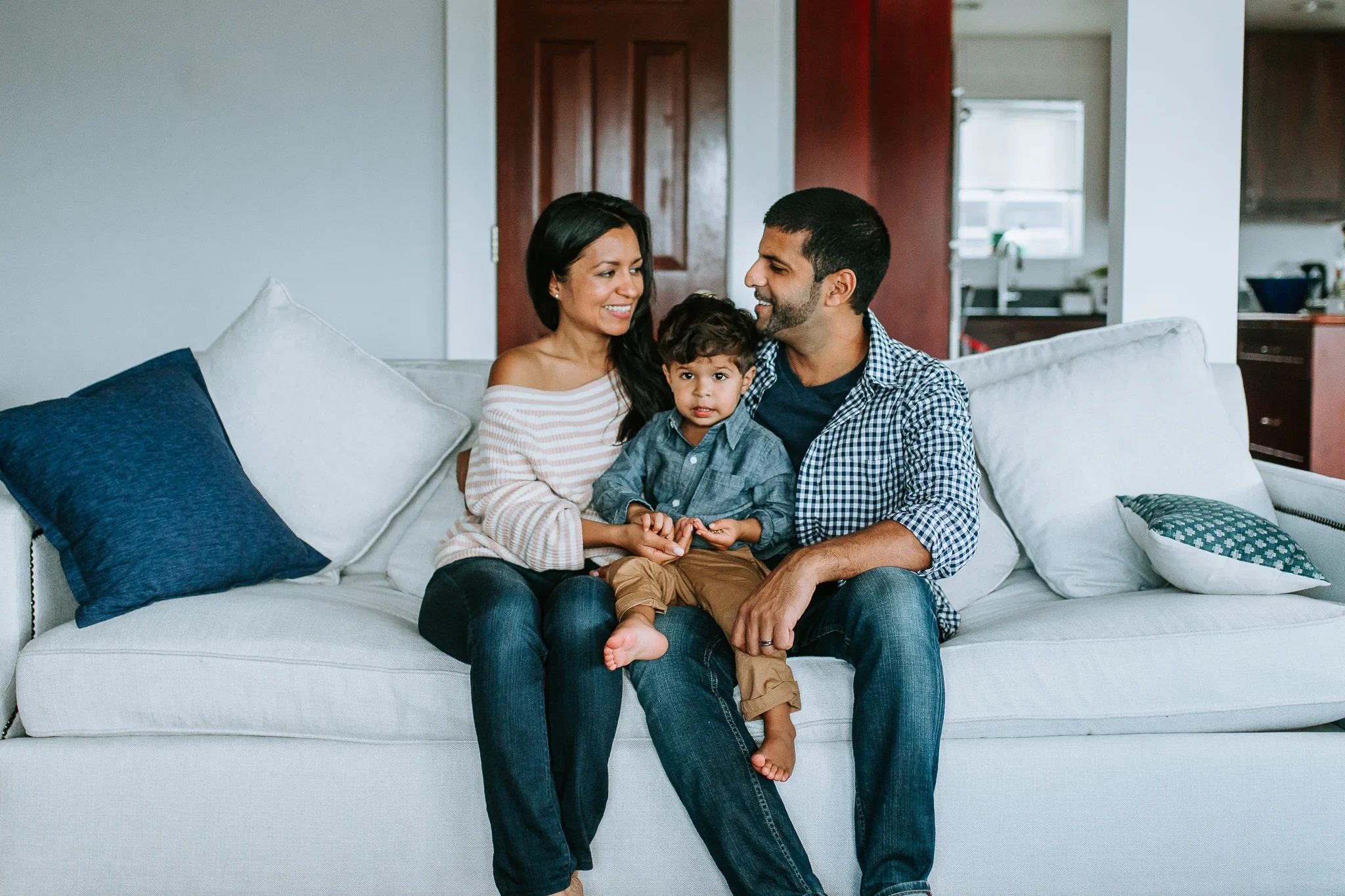 Two adults lean toward a child seated between them on a pale sofa