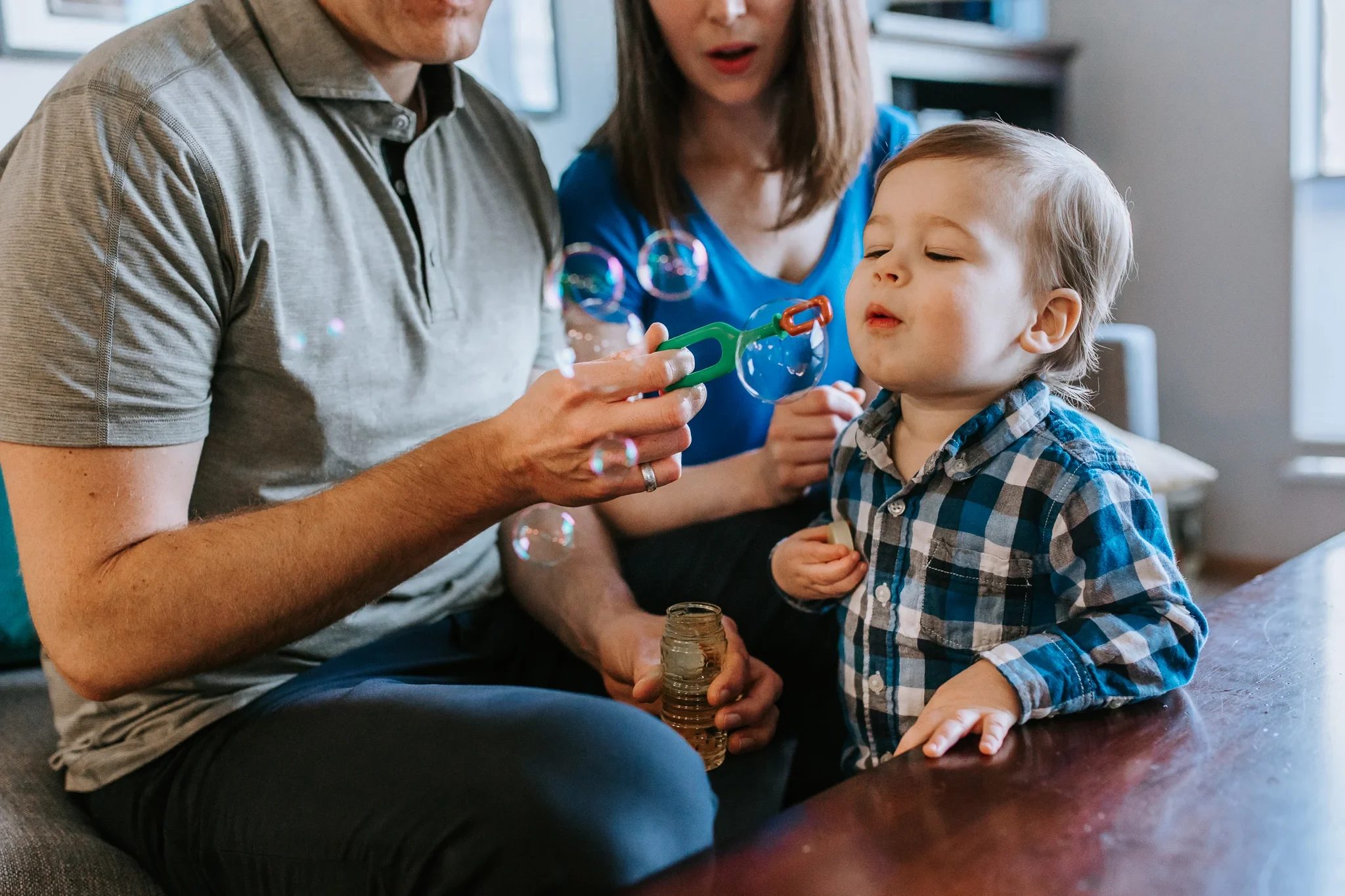 Child watches soap bubbles held between two adults