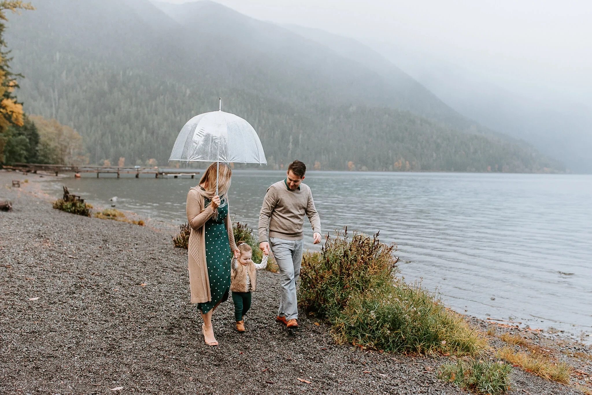 Family walks beside a misty lake beneath a clear umbrella