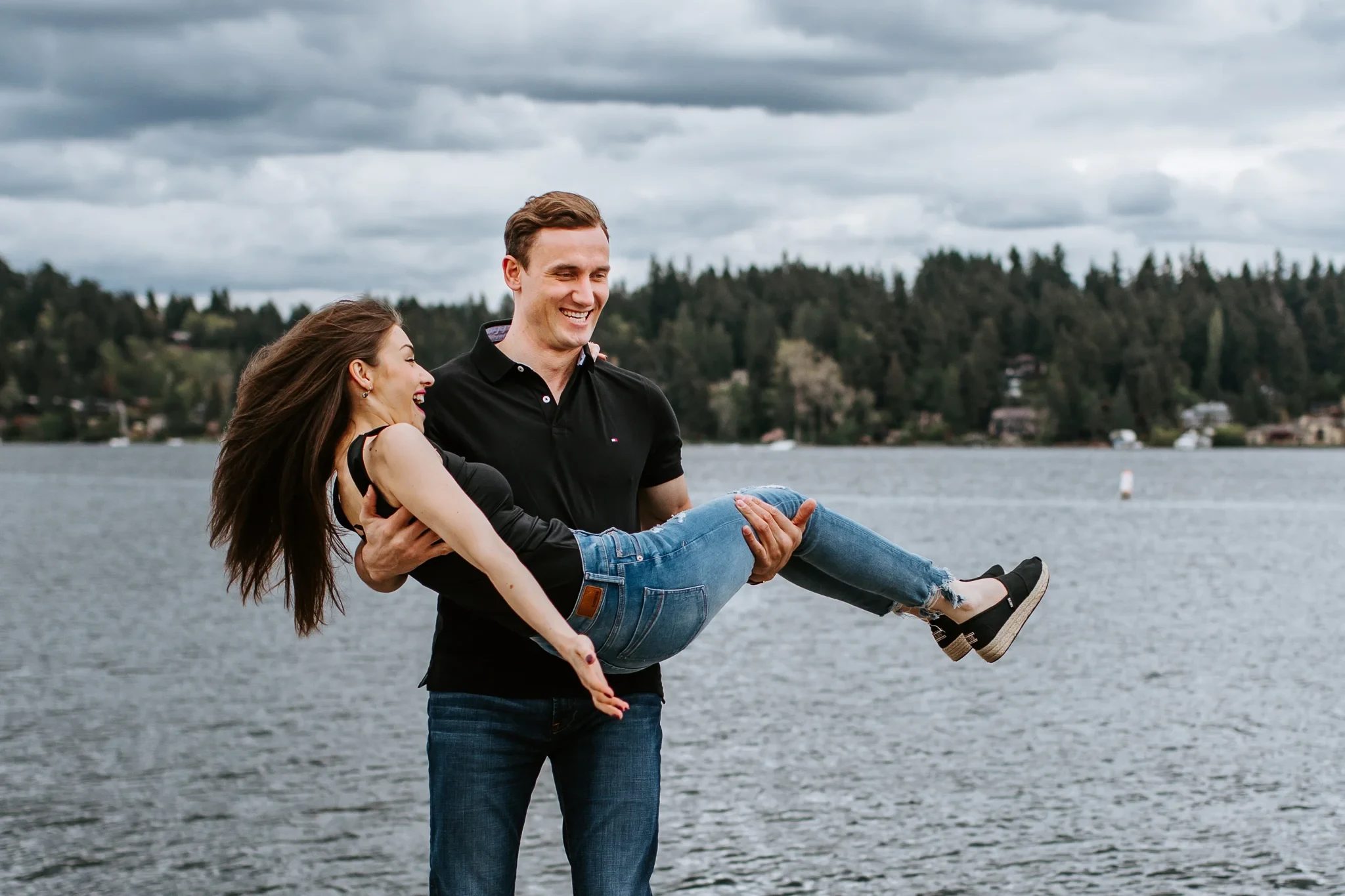 Man carries a smiling woman beside a lake