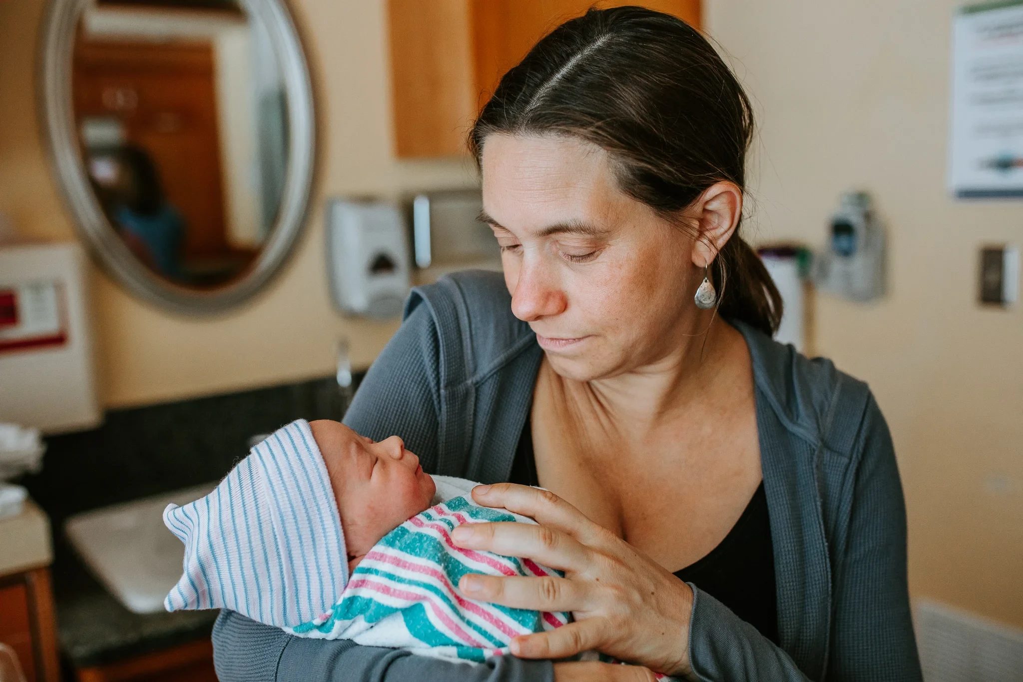 Woman looks down at a baby wrapped in a striped hospital blanket