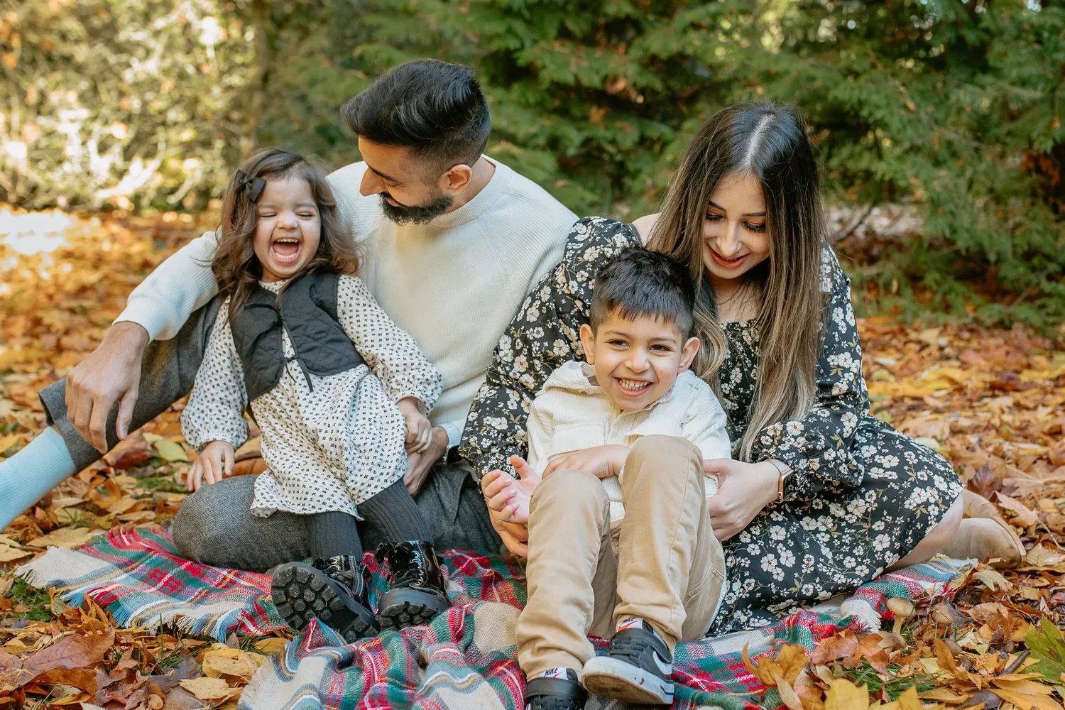 Family laughs together on a blanket beneath autumn trees