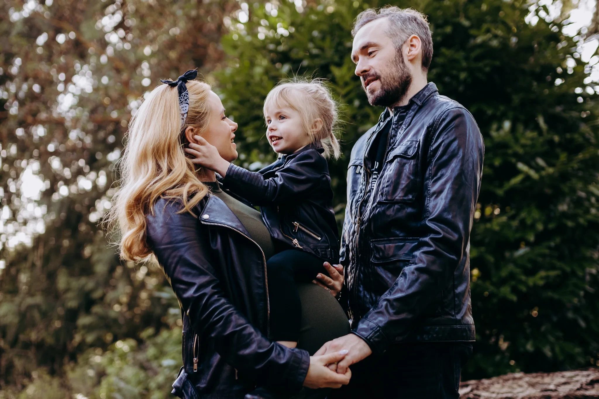 Two adults smile at a child held between them under leafy trees
