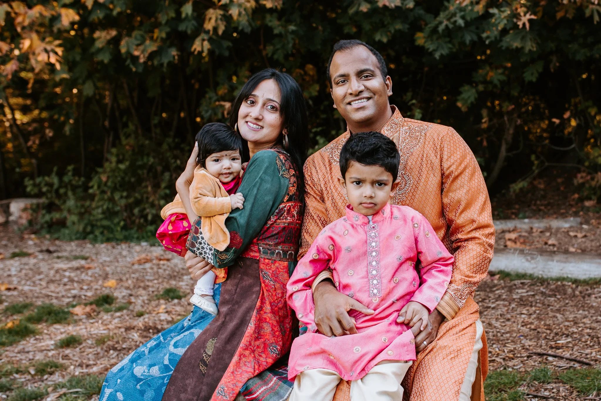 Two adults and two children smile together on a park bench