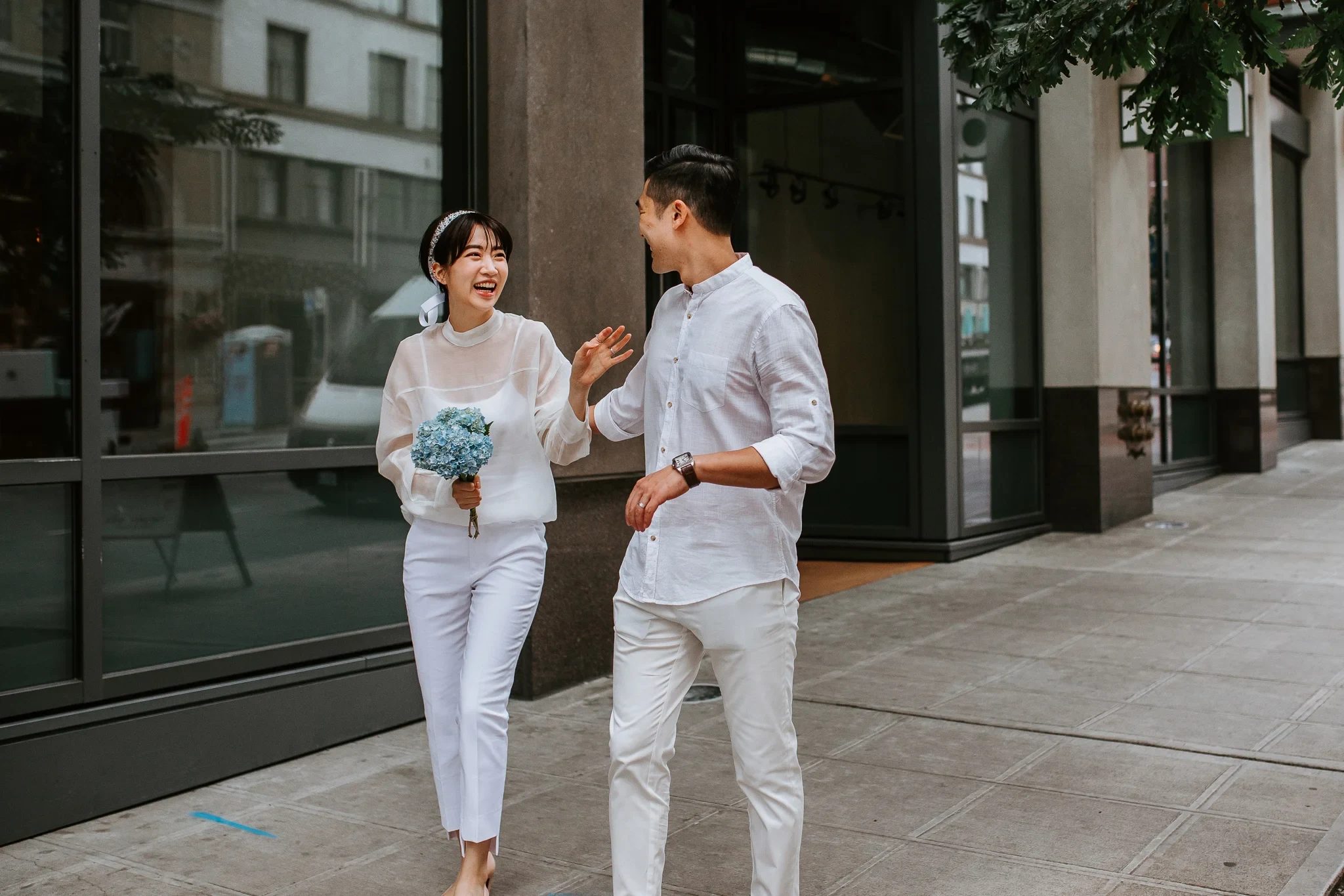 Two adults in white clothing talk while standing on a city sidewalk