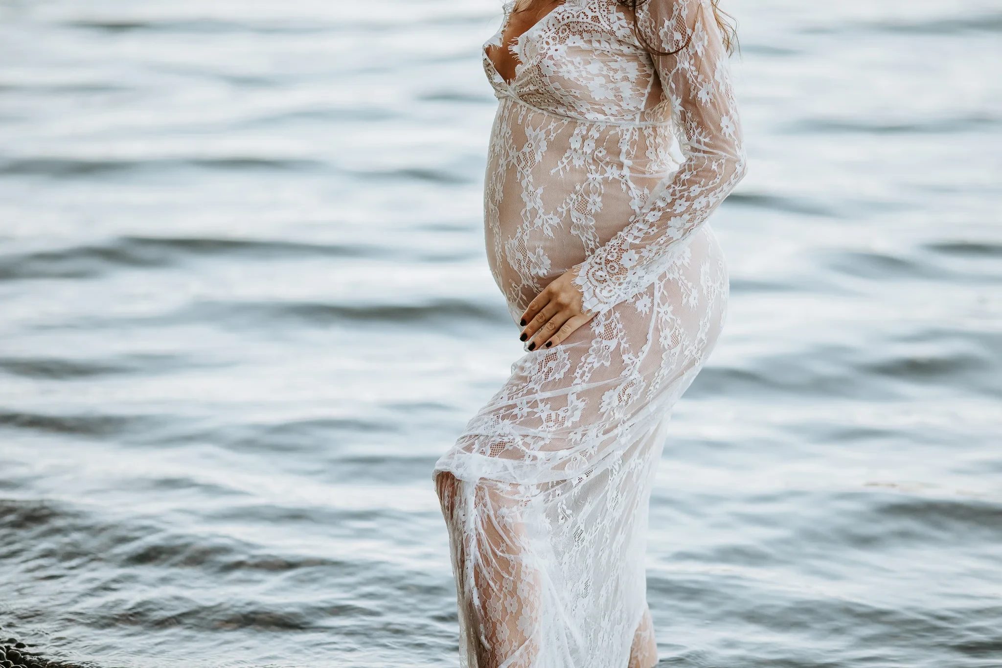 Detail of a pale lace gown beside softly rippling water