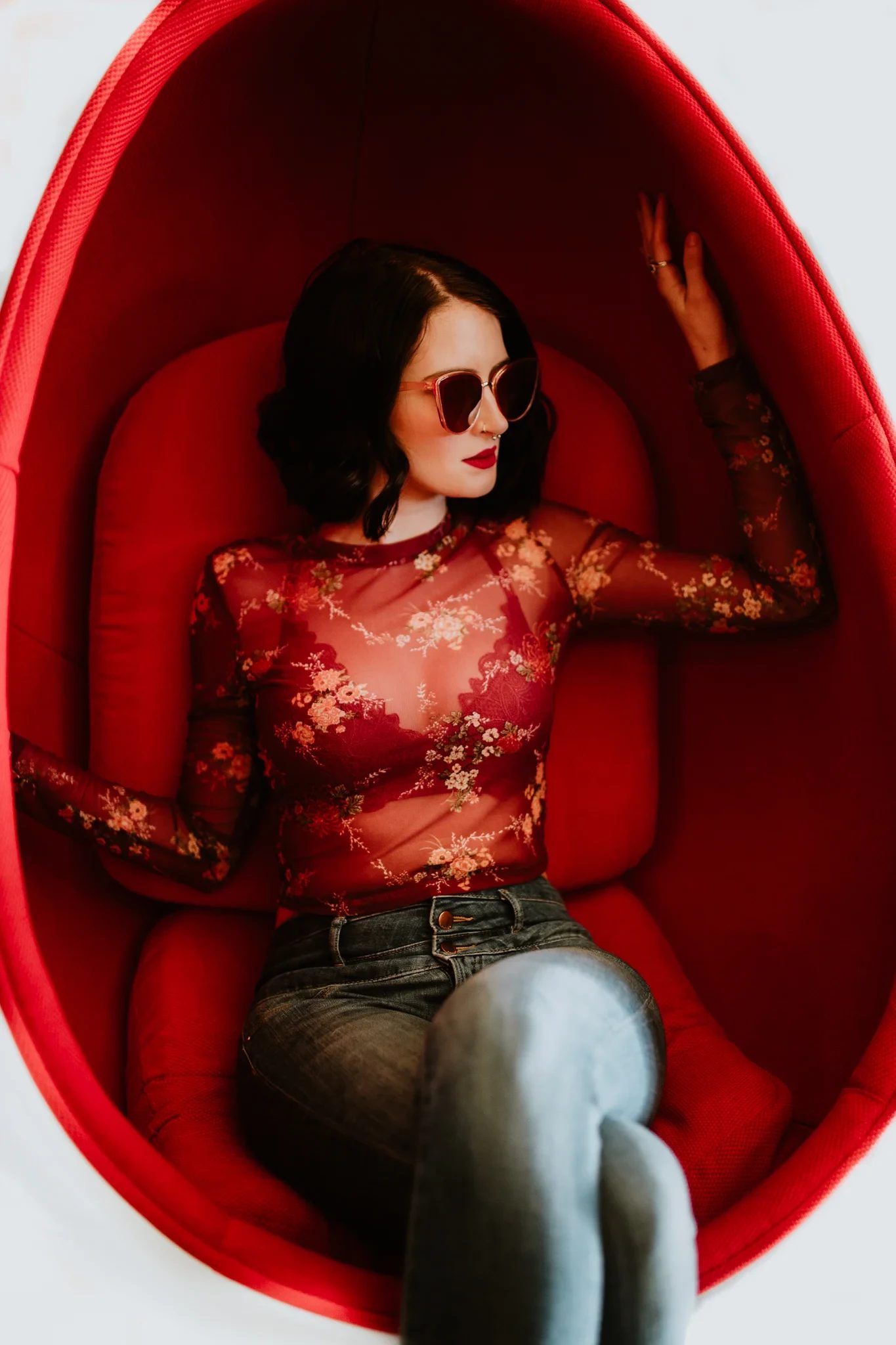 Woman wearing sunglasses sits in a bright red pod chair