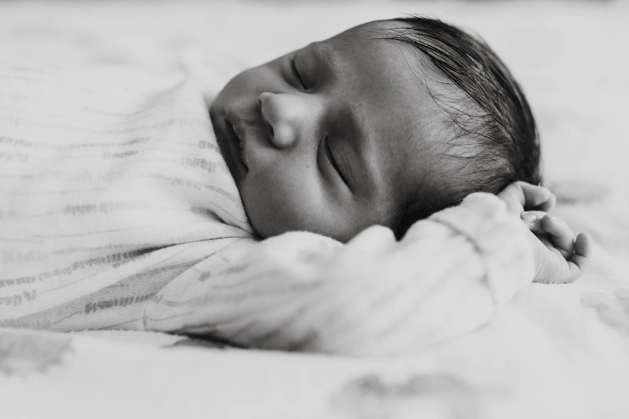 Black-and-white close-up of a sleeping baby’s face and raised hand