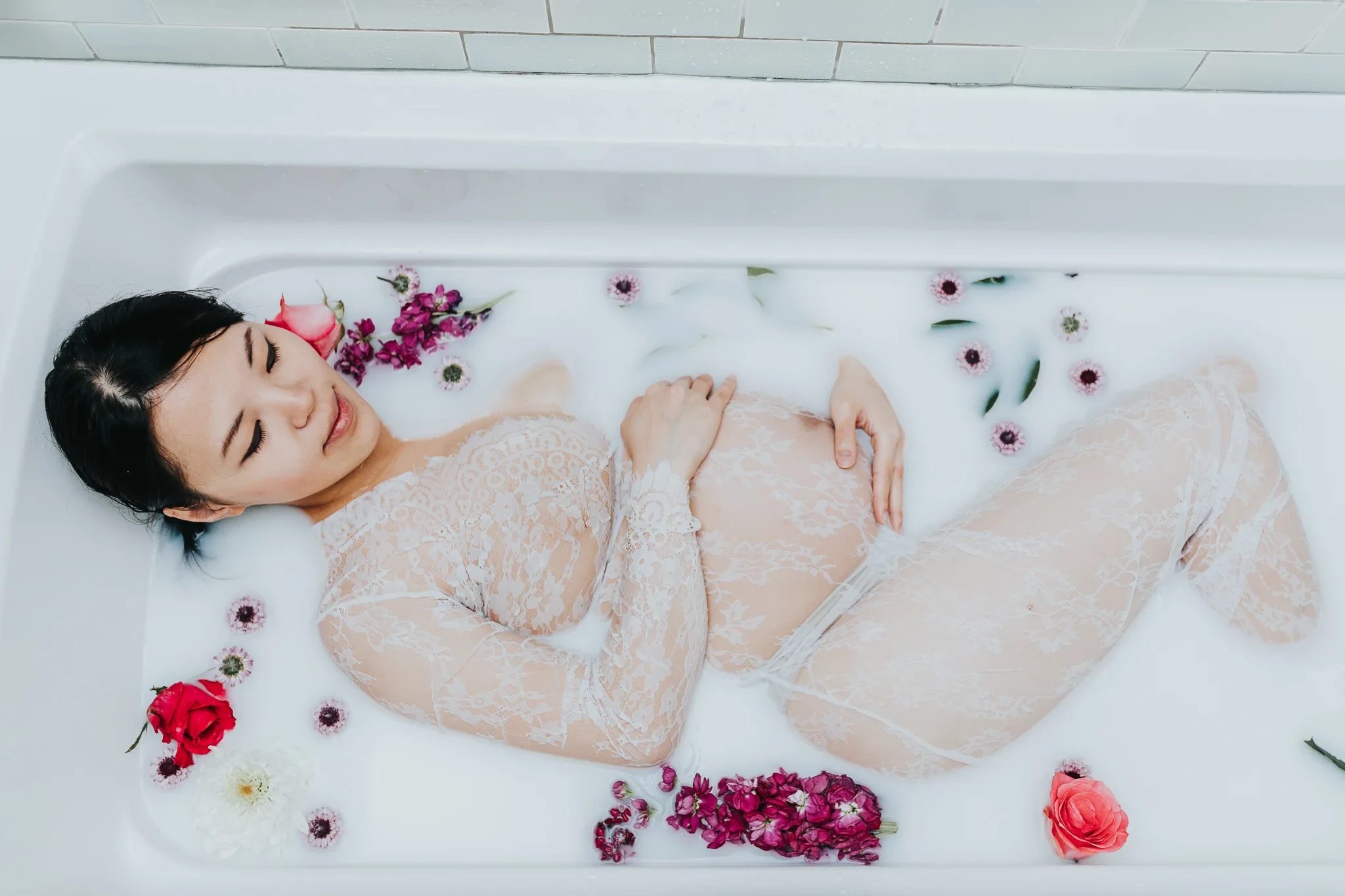 Woman in a pale lace dress reclines in white water with scattered flowers