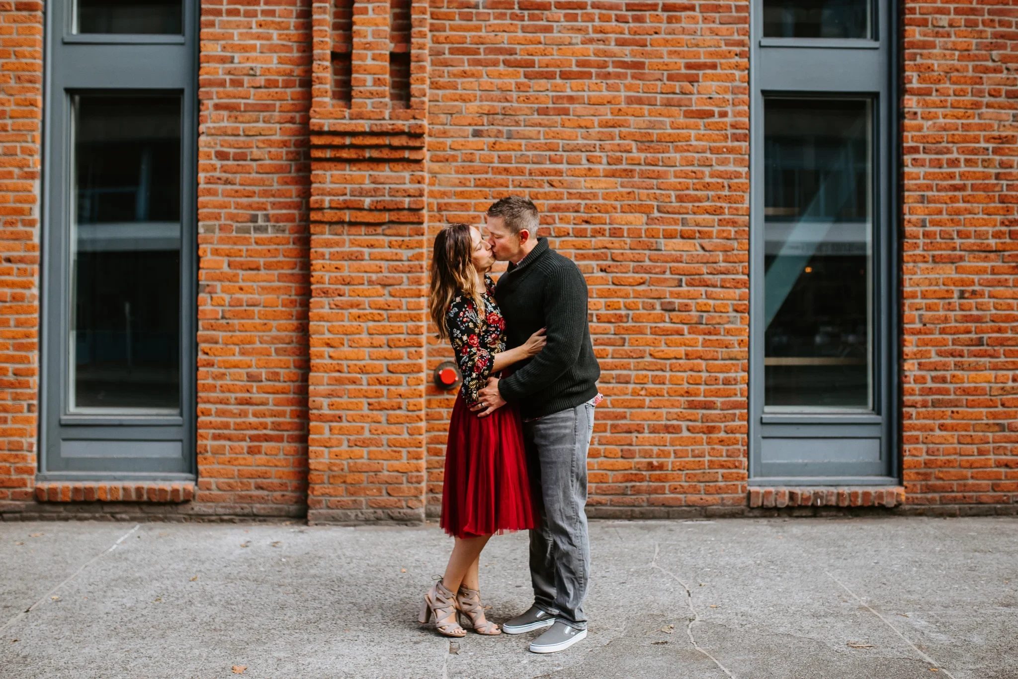 Two adults kiss in front of a red brick wall