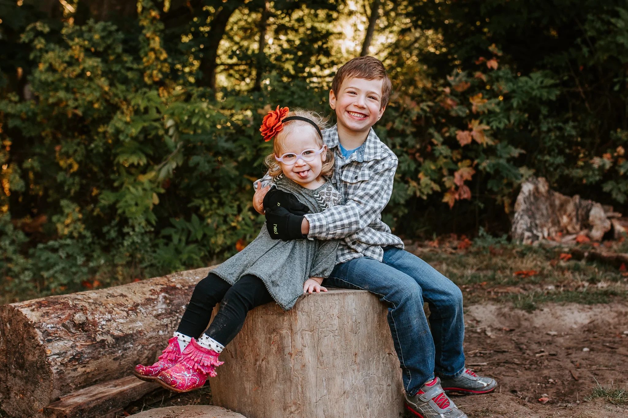 Two children embrace while sitting on a tree stump