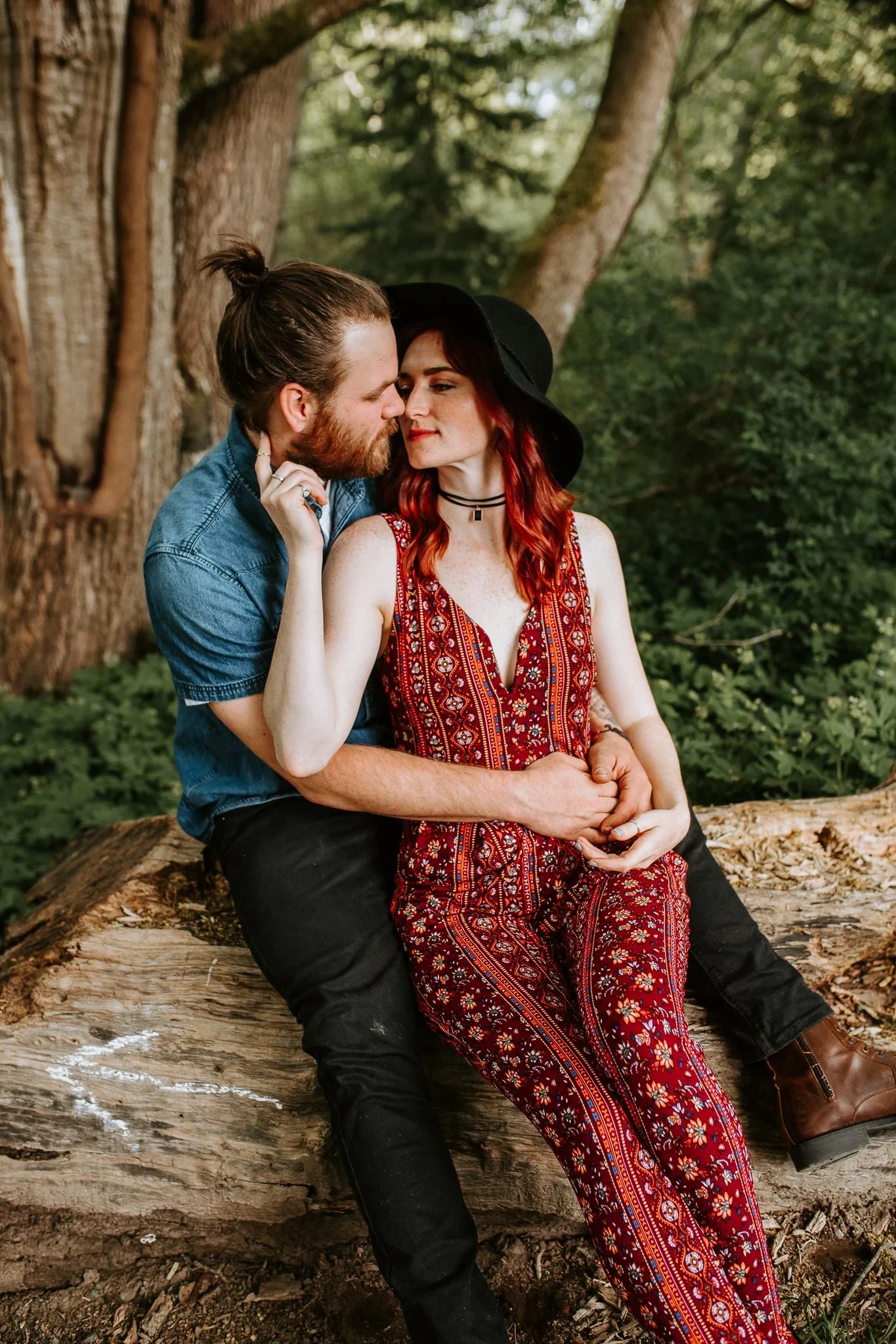 Two adults sit together against a wide tree trunk
