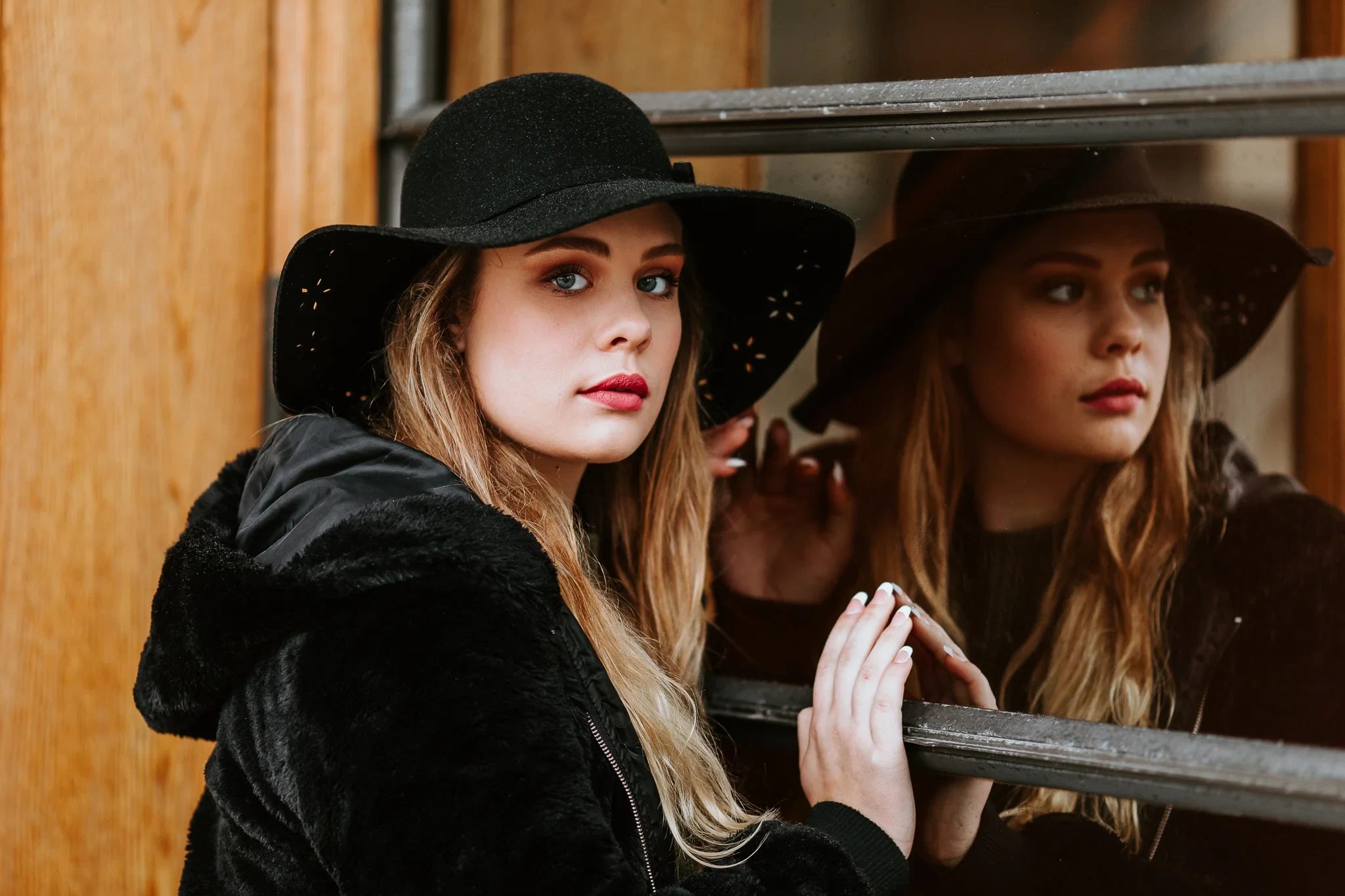 Woman in a black hat looks beside her reflection in a window