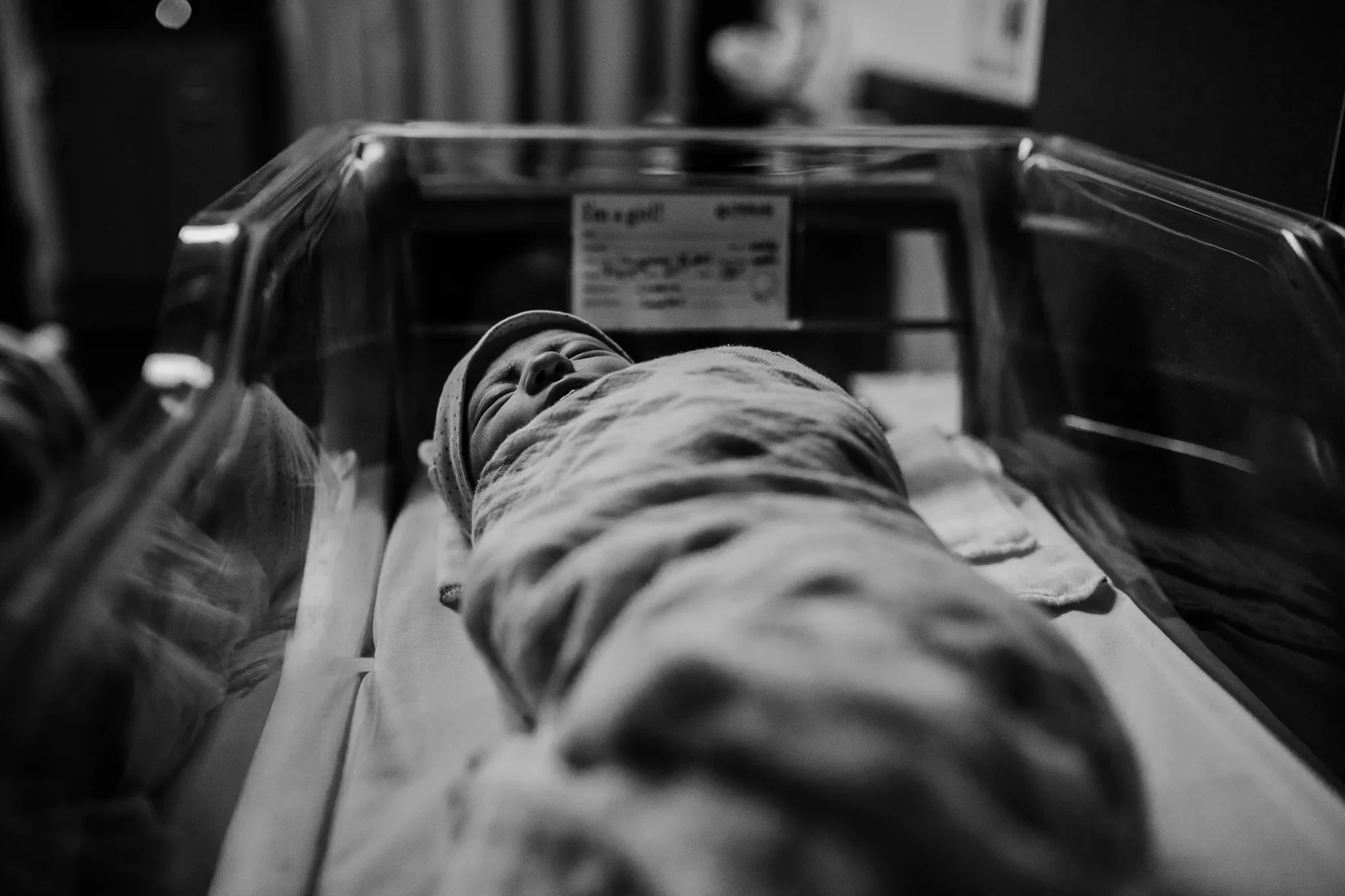 Black-and-white view along a clear bassinet toward a sleeping baby