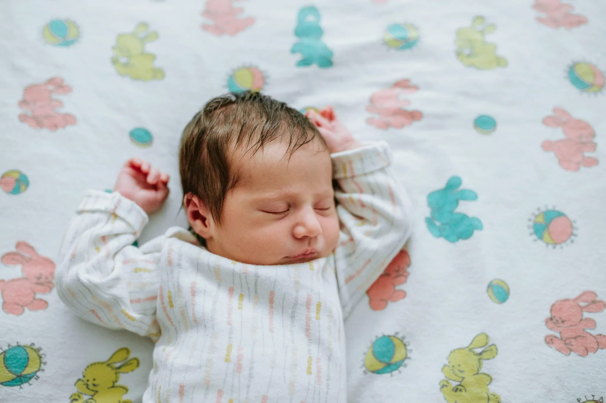 Sleeping baby in a striped outfit lies on a colorful patterned blanket