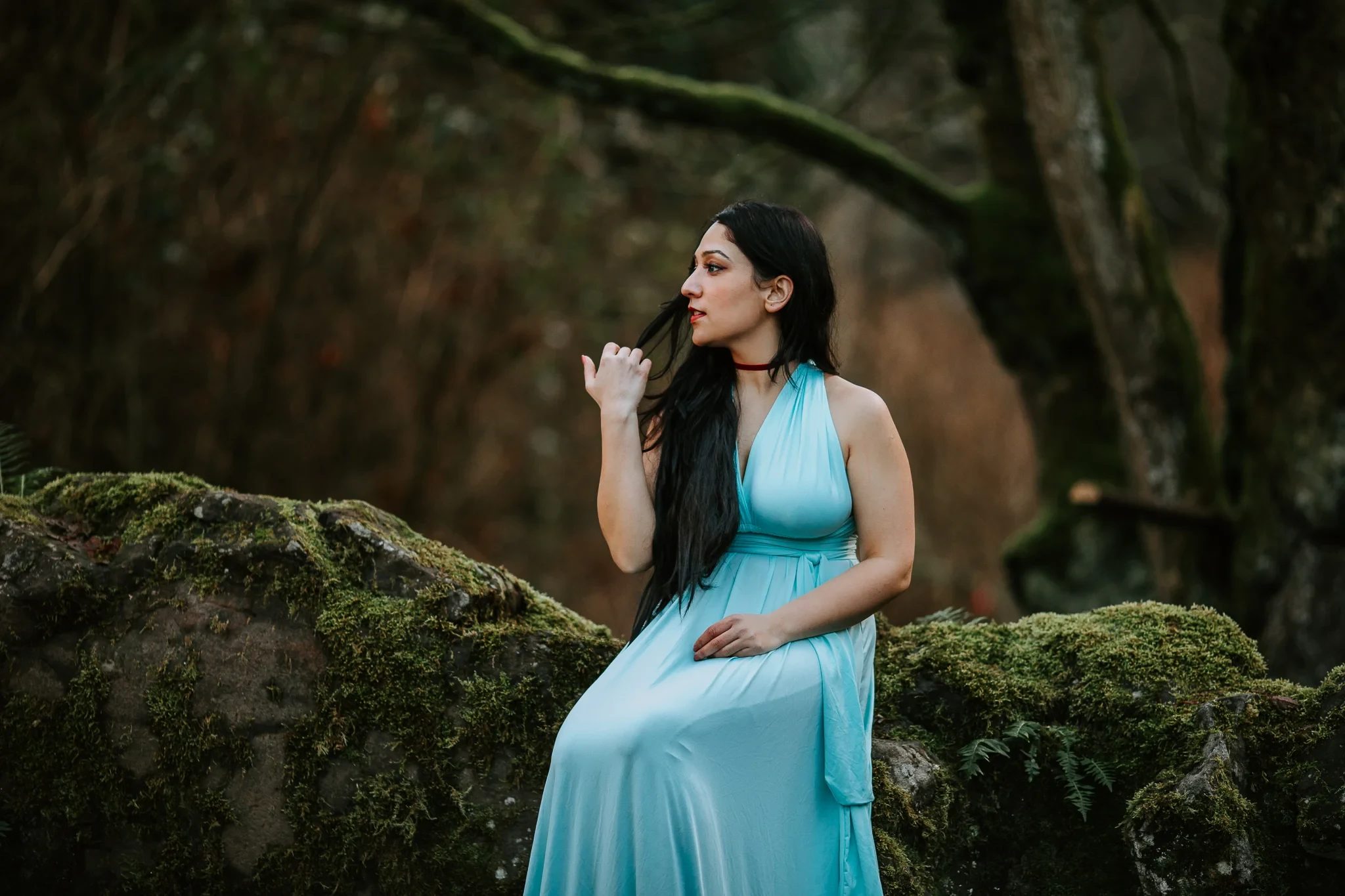 Woman in a turquoise dress sits on a moss-covered rock