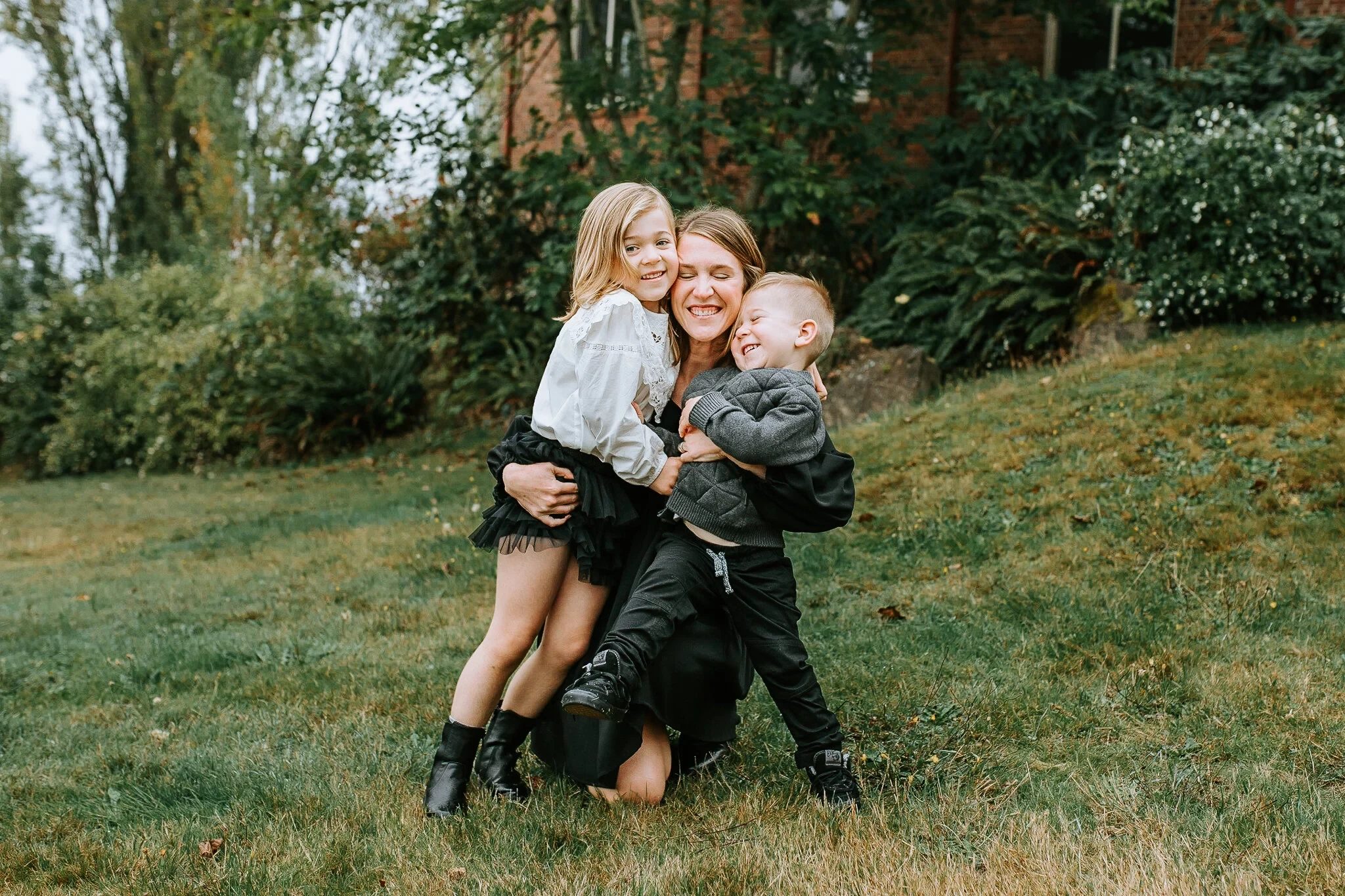 Woman kneeling on a lawn embraces two smiling children