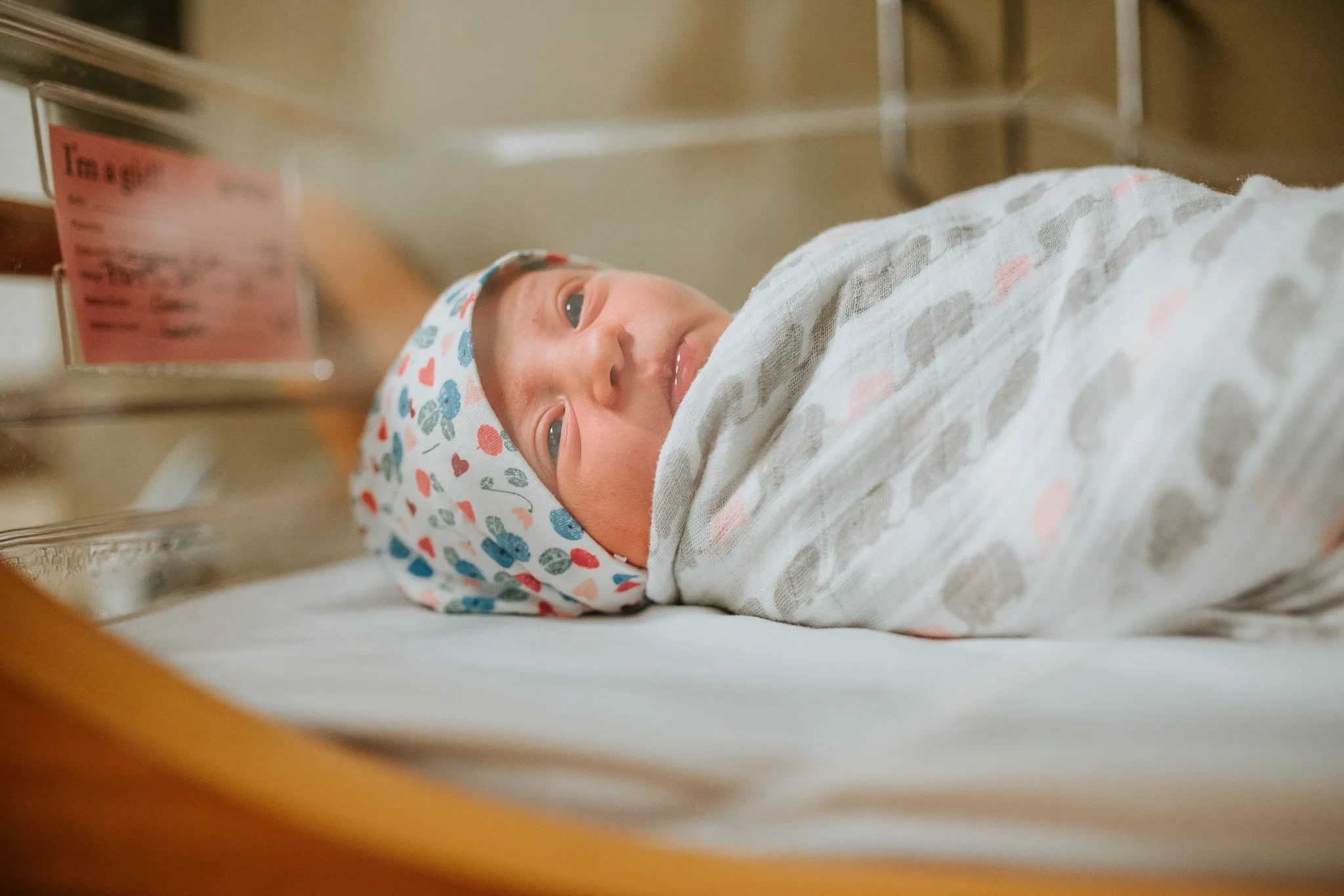 Baby in a patterned cap rests wrapped in a white hospital blanket