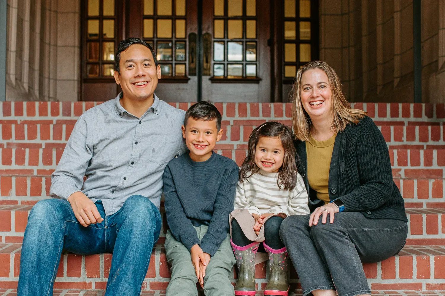 Family sits together on brick steps in front of a doorway