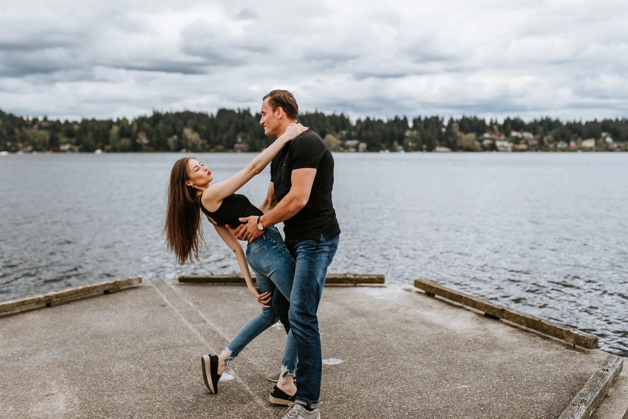 Man dips a woman backward beside a lake