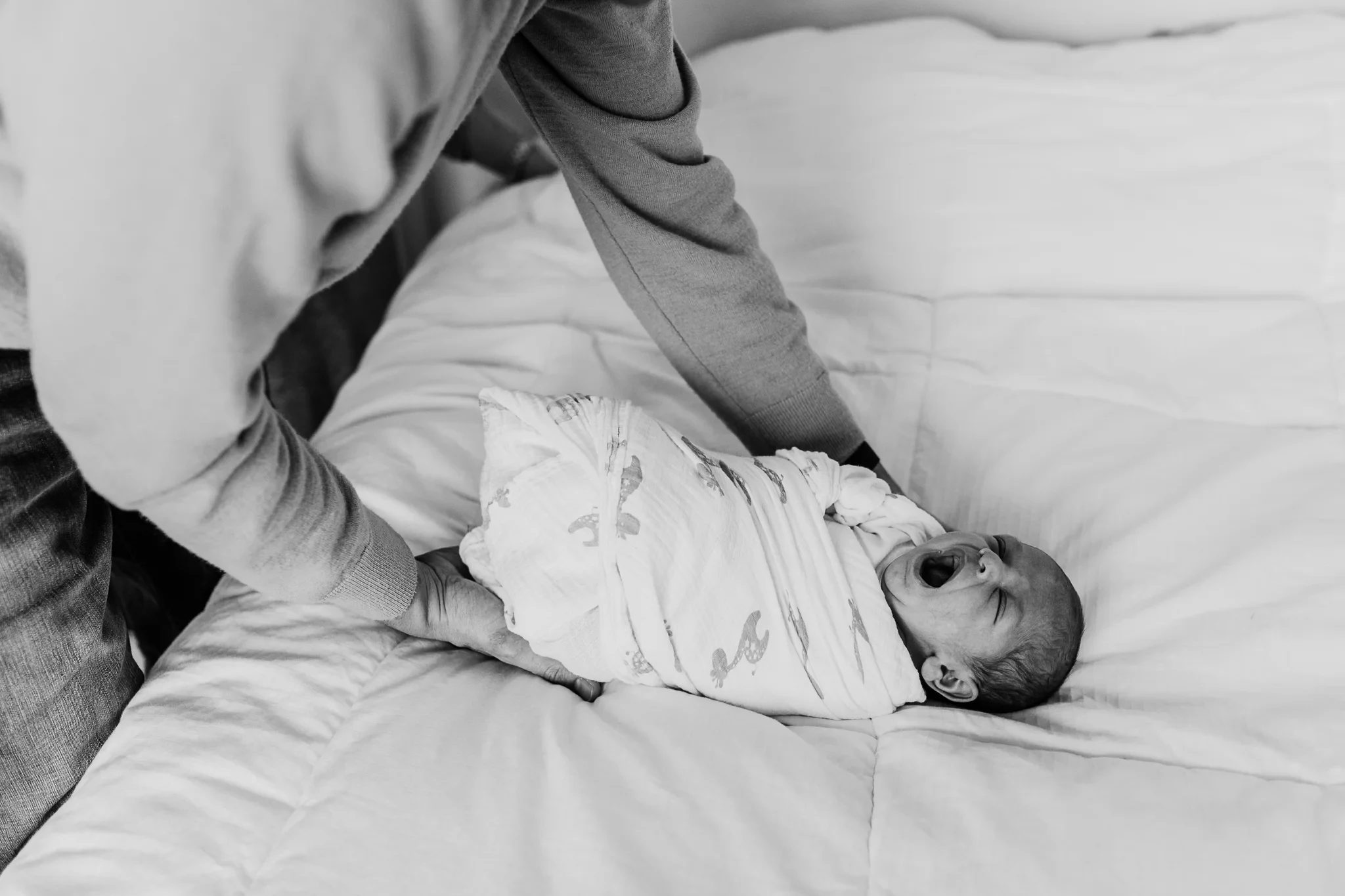 Black-and-white photograph of an adult wrapping a baby on a bed