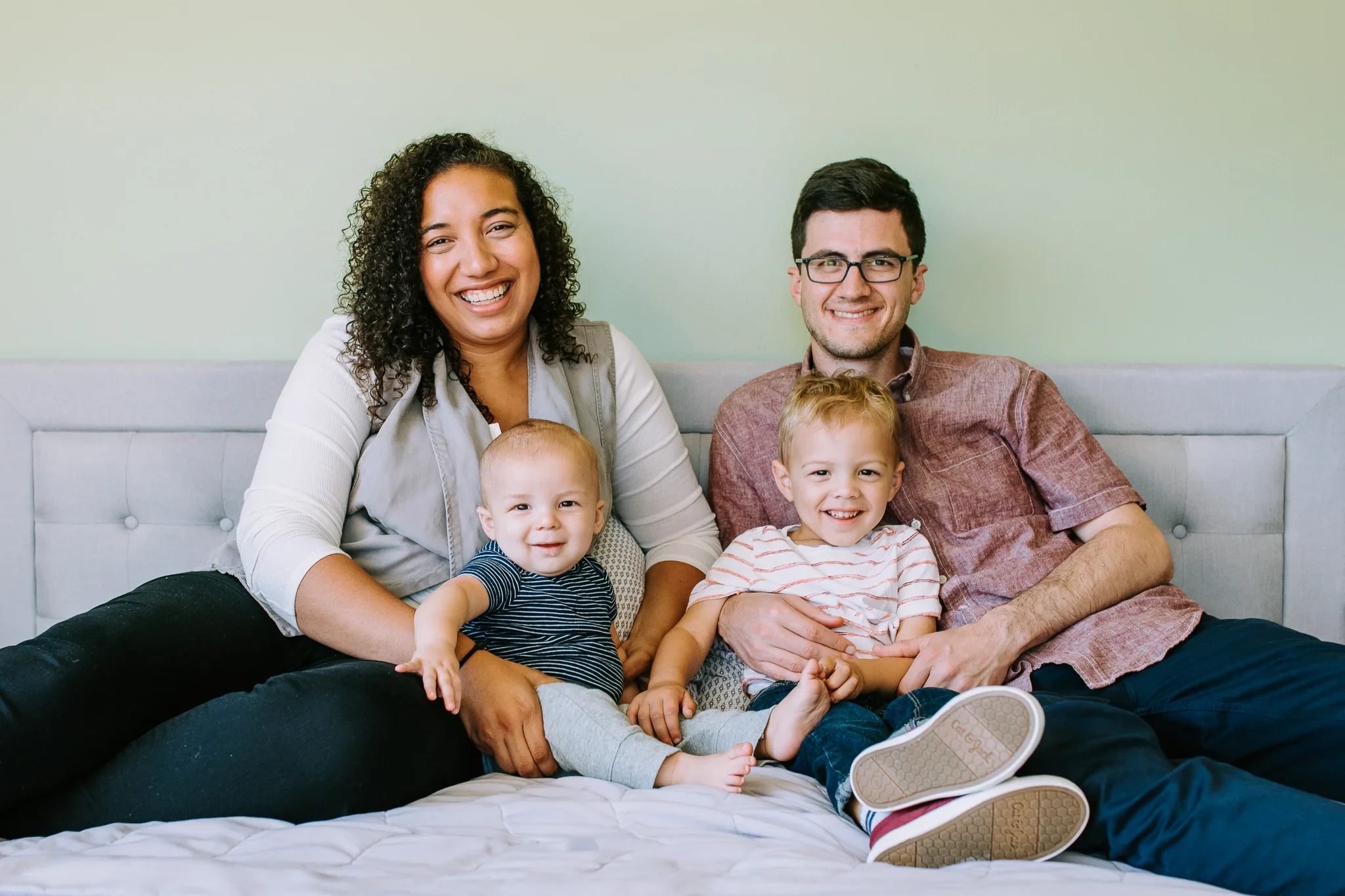 Two adults and two children sit together on a bed