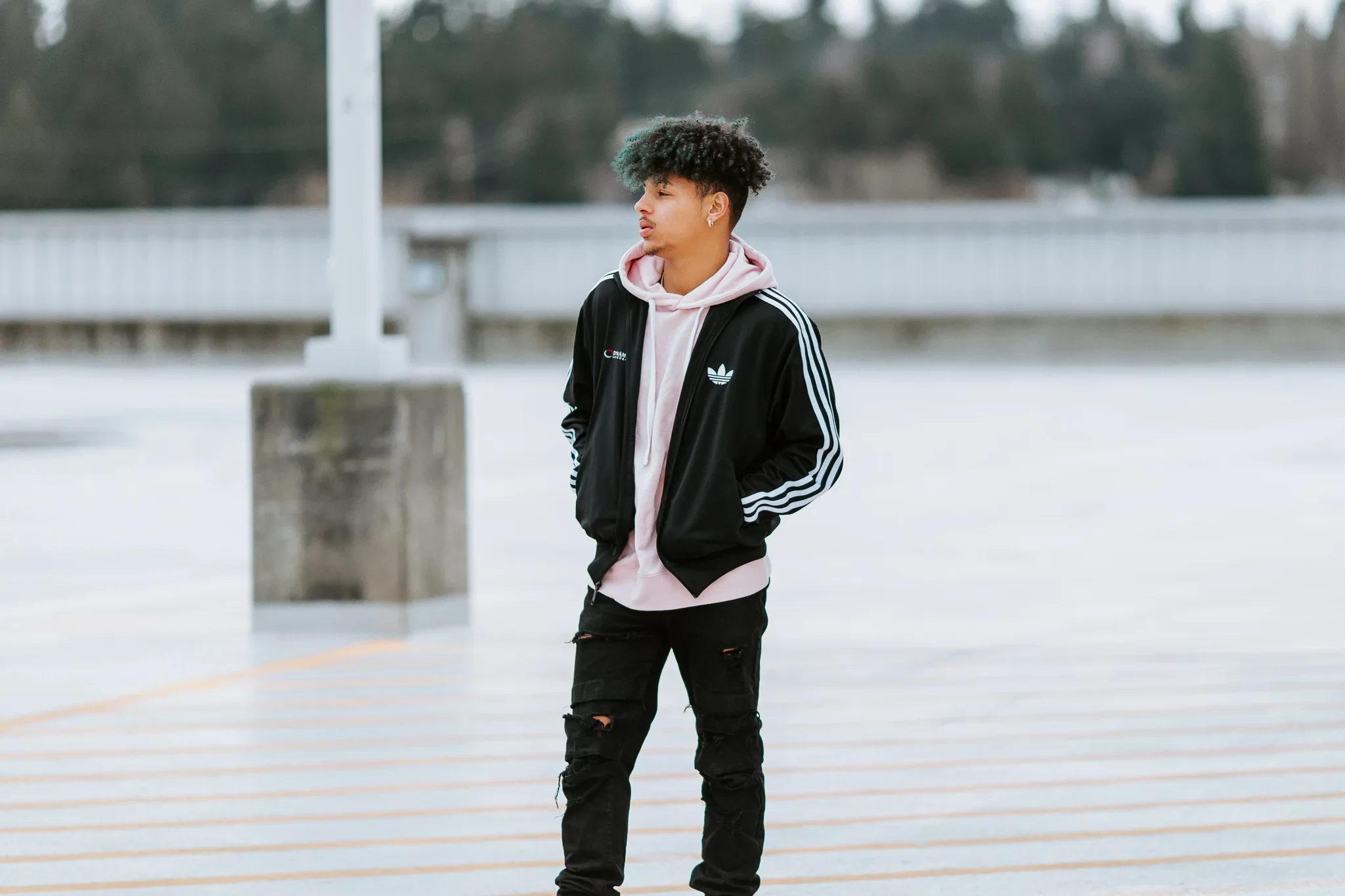 Young person in a dark jacket stands on a waterfront boardwalk