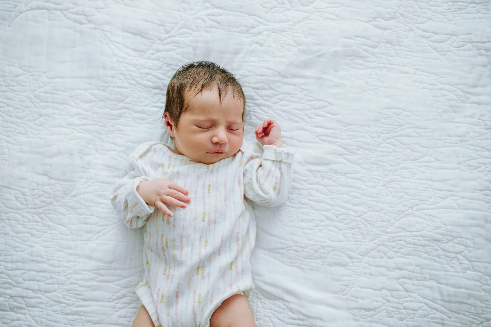 Sleeping baby stretches one arm on a textured pale blanket