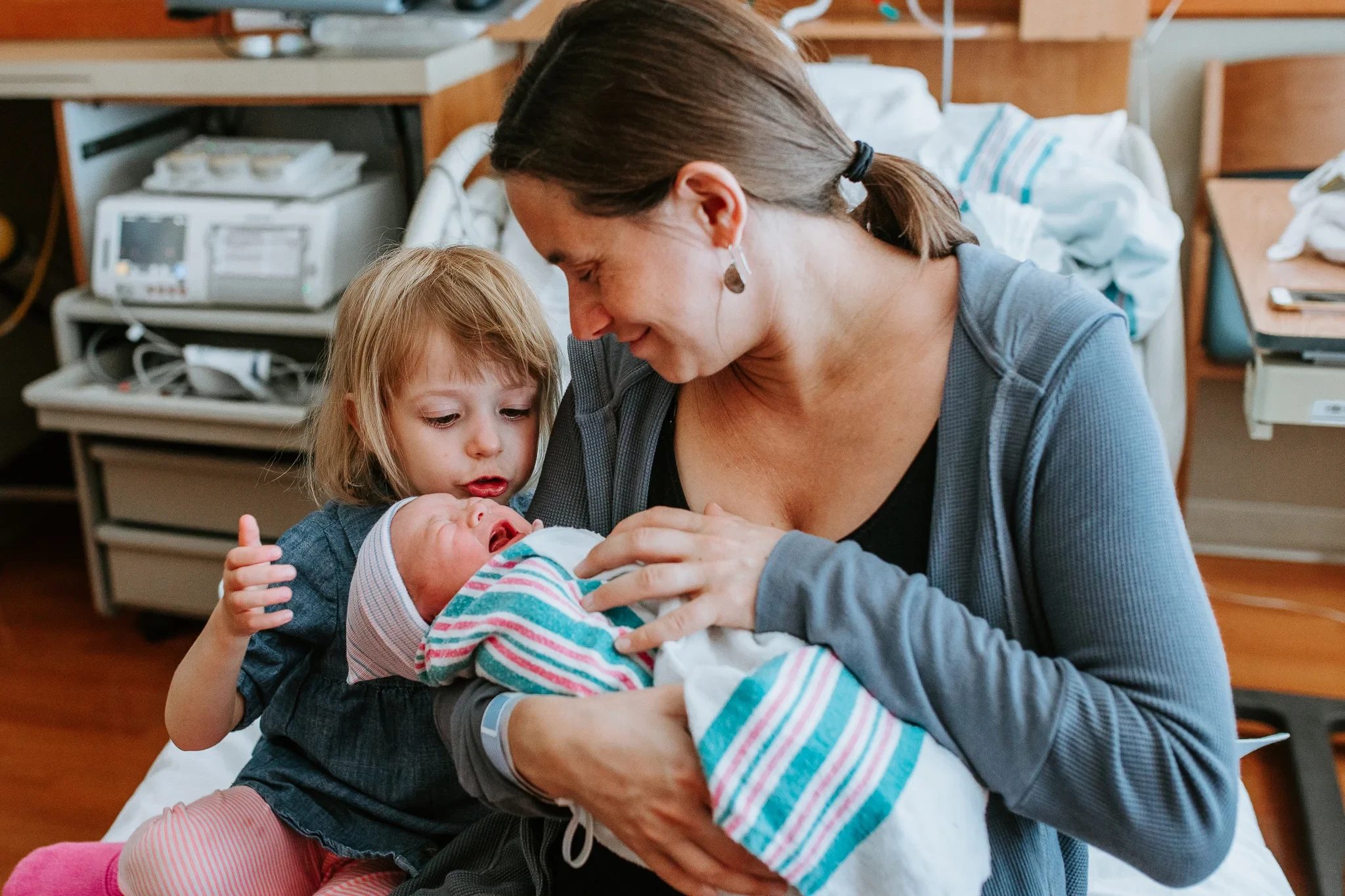 Woman and child look at a baby wrapped in a striped blanket