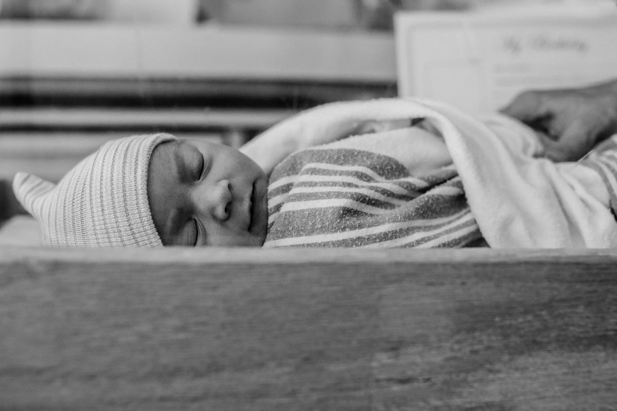 Black-and-white photograph of a swaddled baby lying on a bed