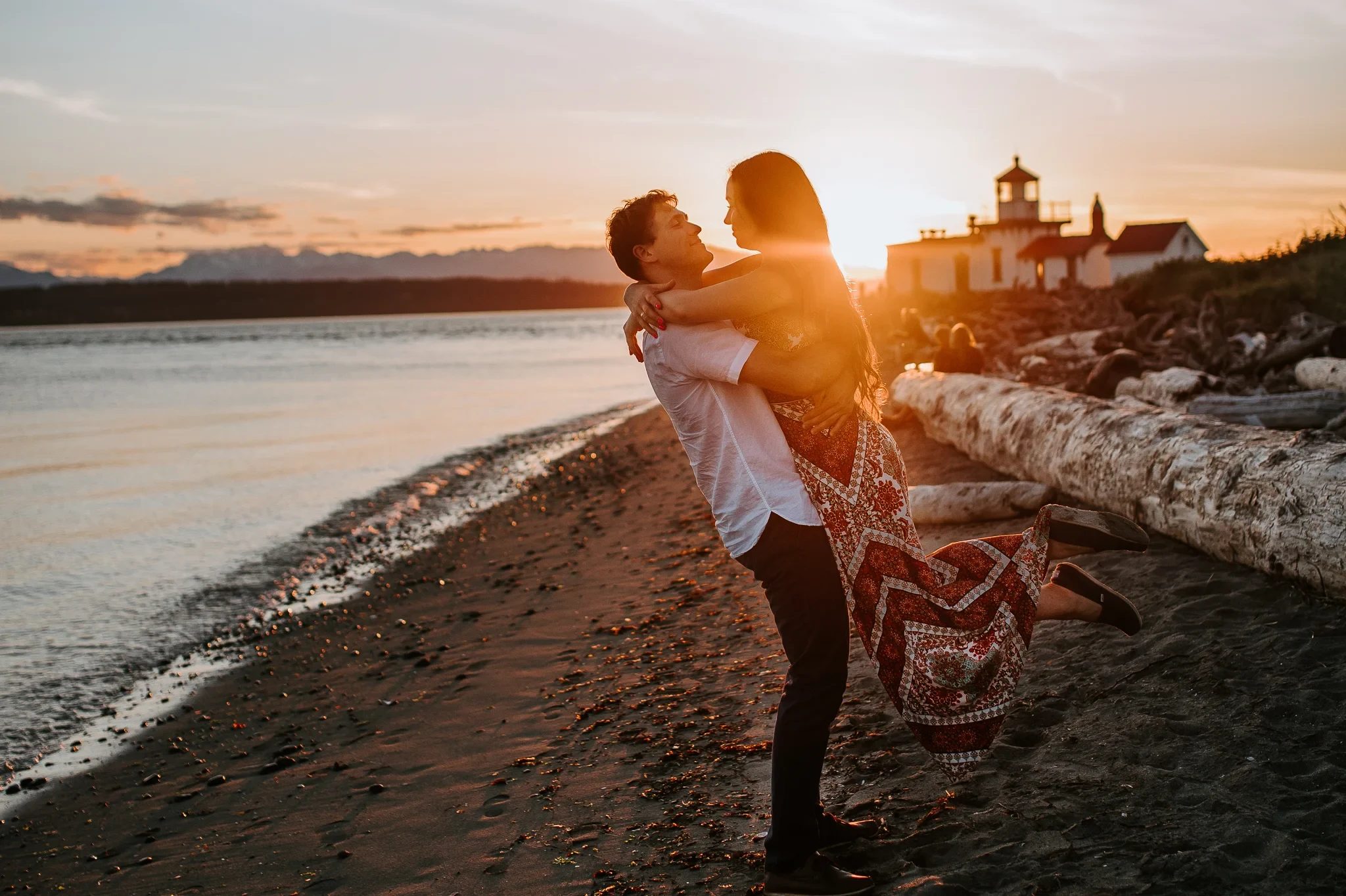 Two adults embrace on the beach with the setting sun between them