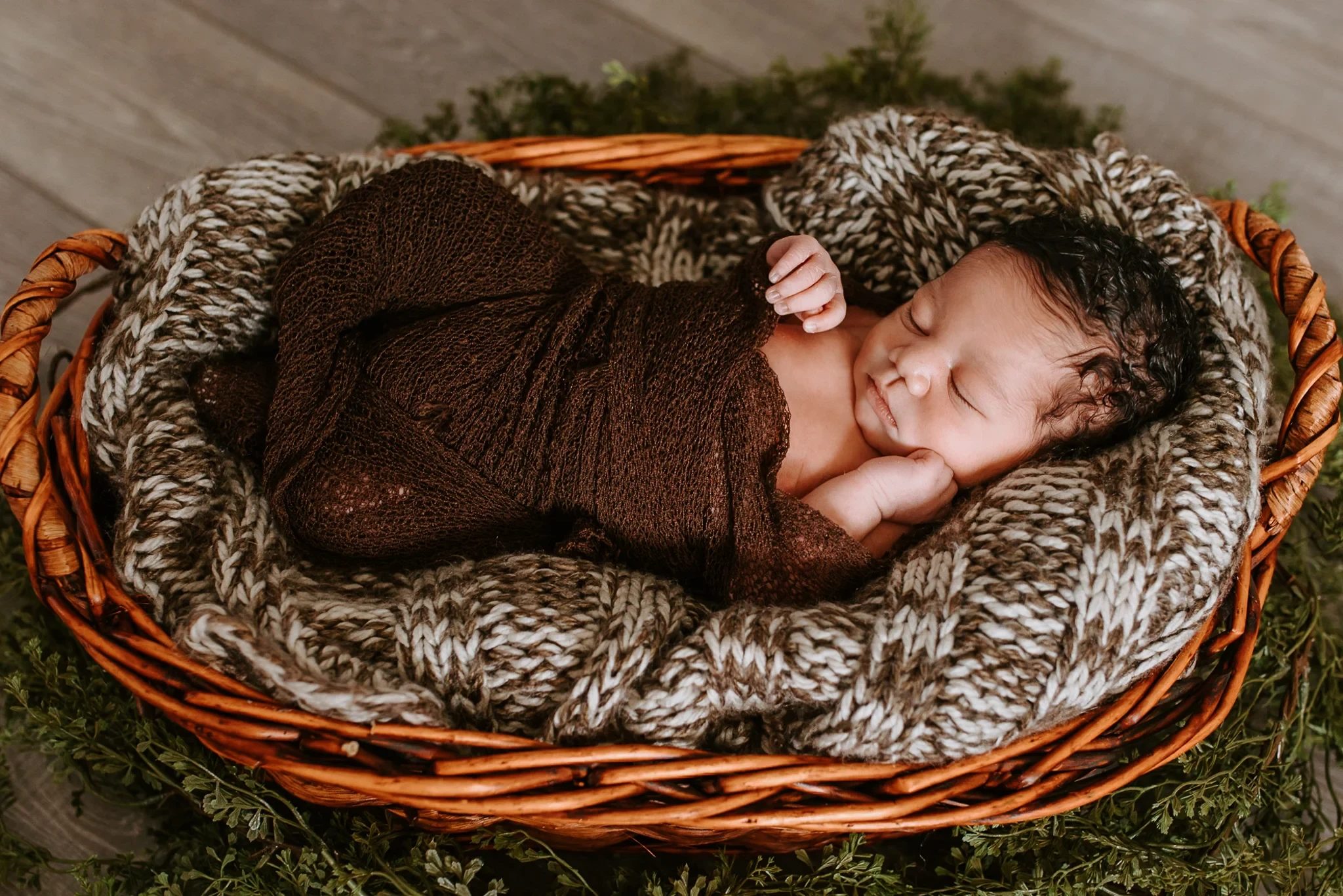 Sleeping baby curled in a brown wrap inside a woven basket