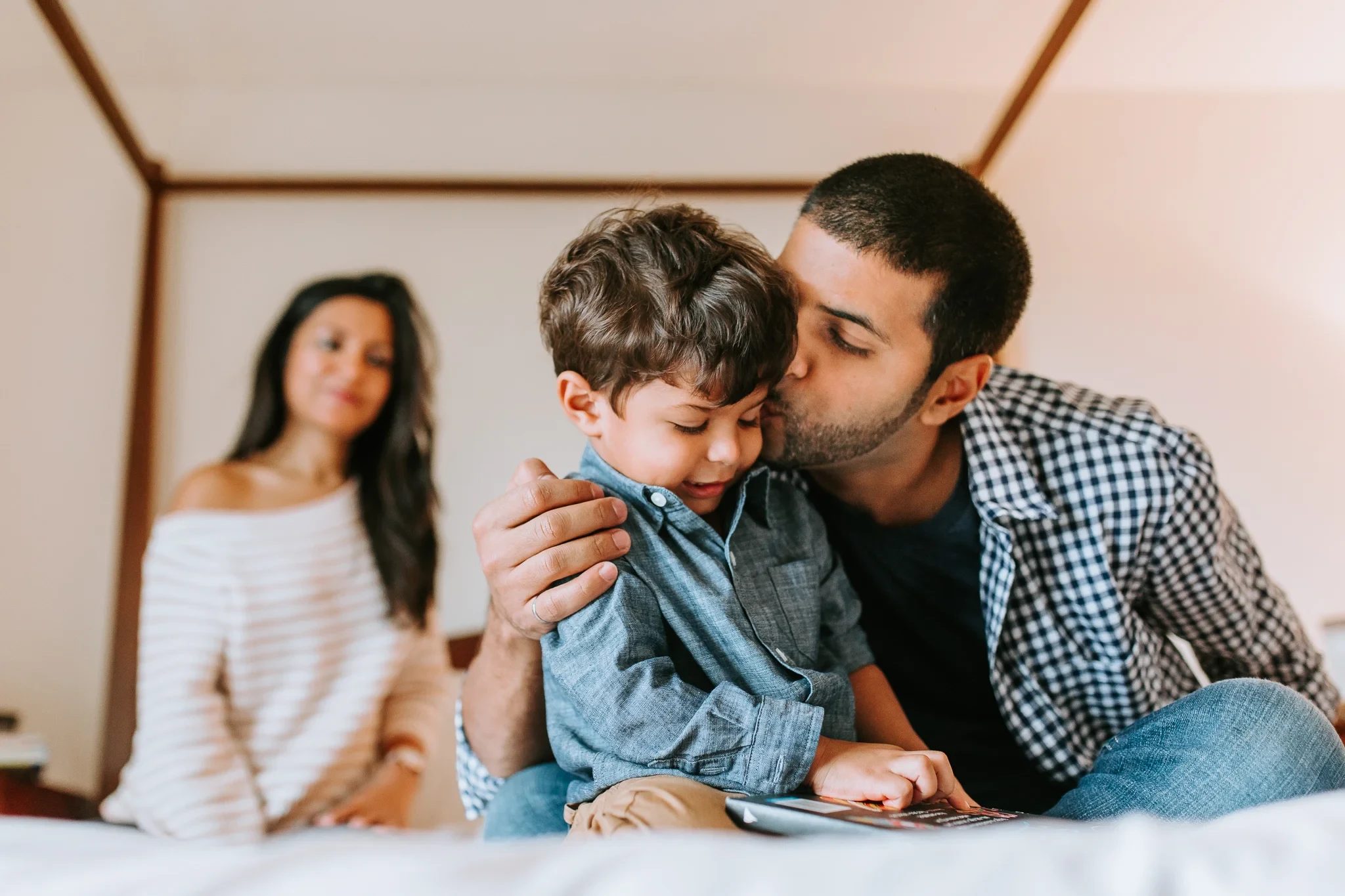Man kisses a child sitting on his lap on a bed