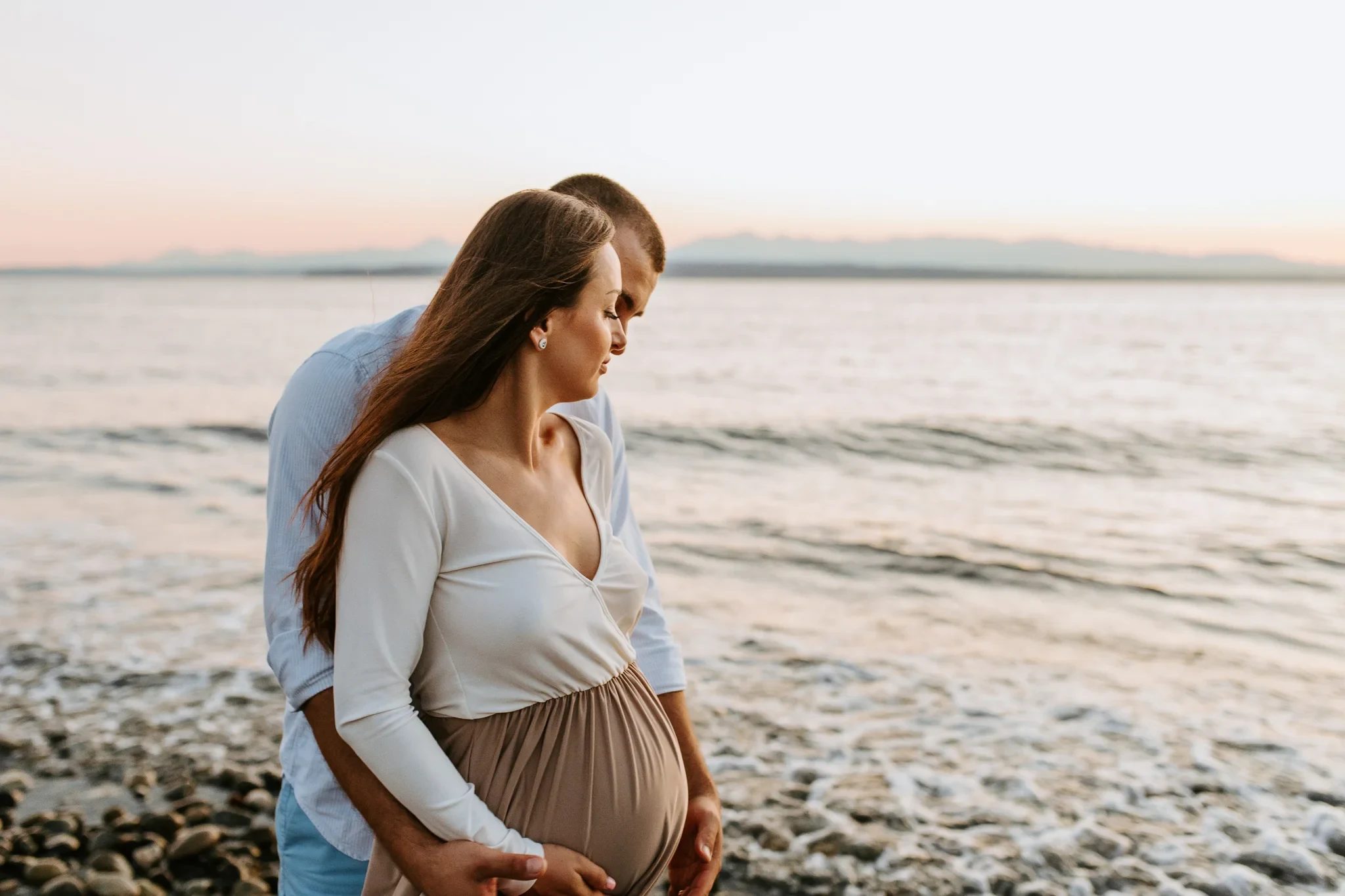 Woman in a pale wrap top and taupe skirt stands beside calm water