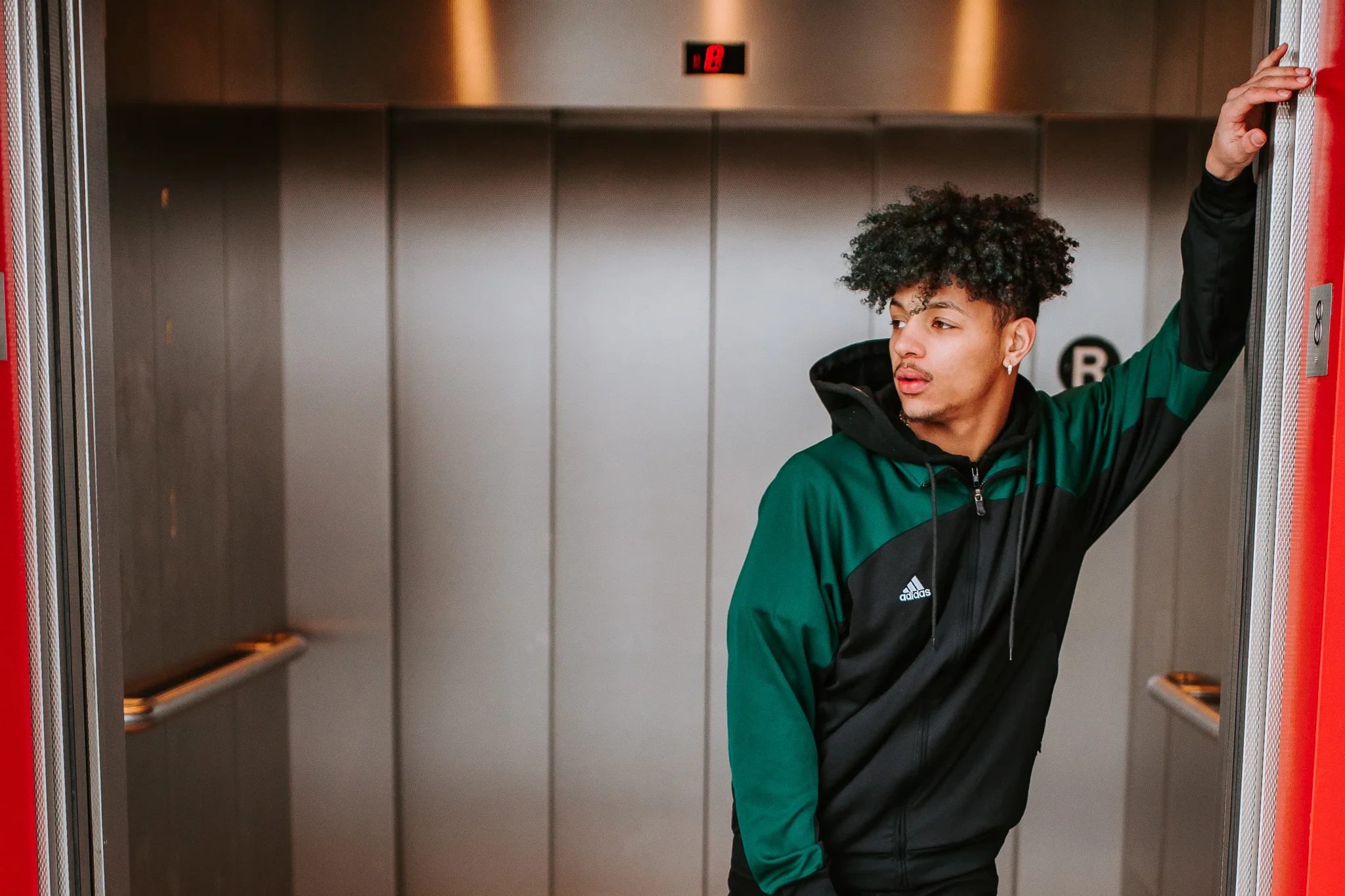 Young person in a green hoodie stands in an elevator doorway