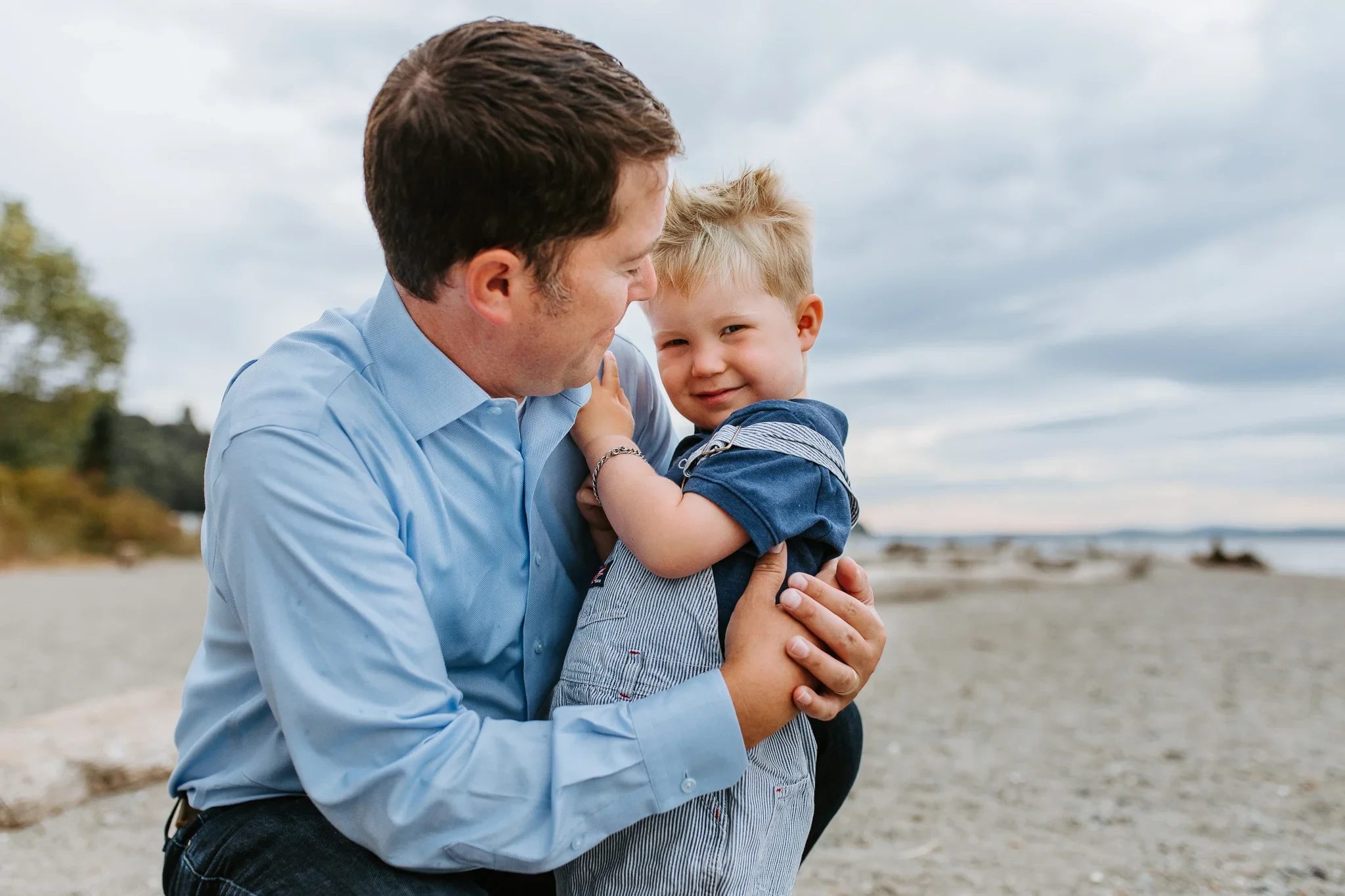 Man in a blue shirt holds a laughing child on the beach