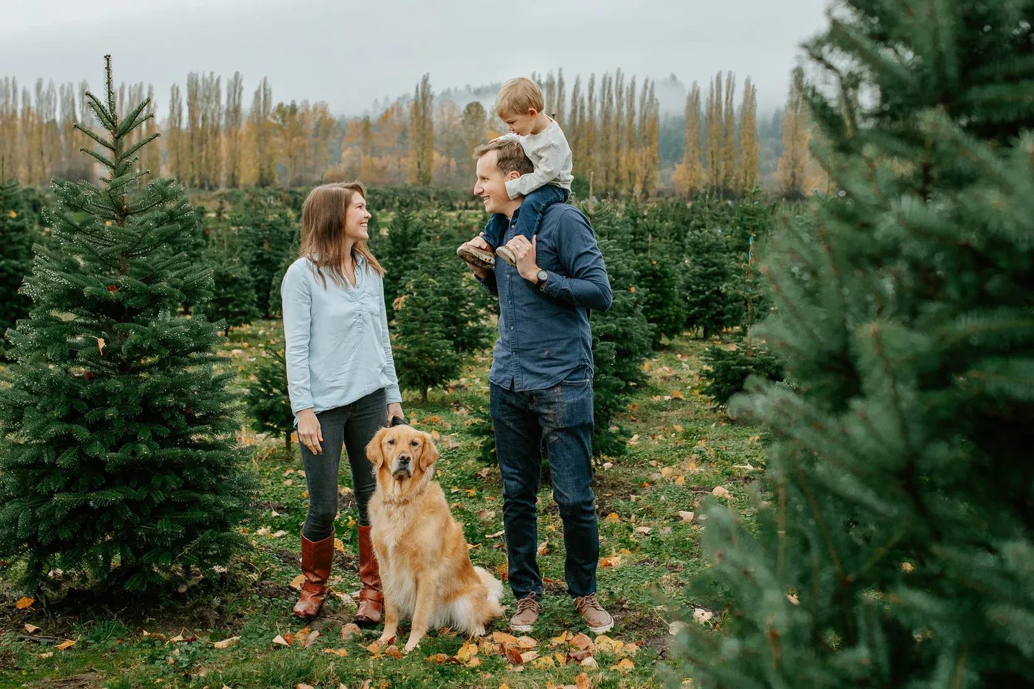 Two adults and a child stand beside a dog at a tree farm