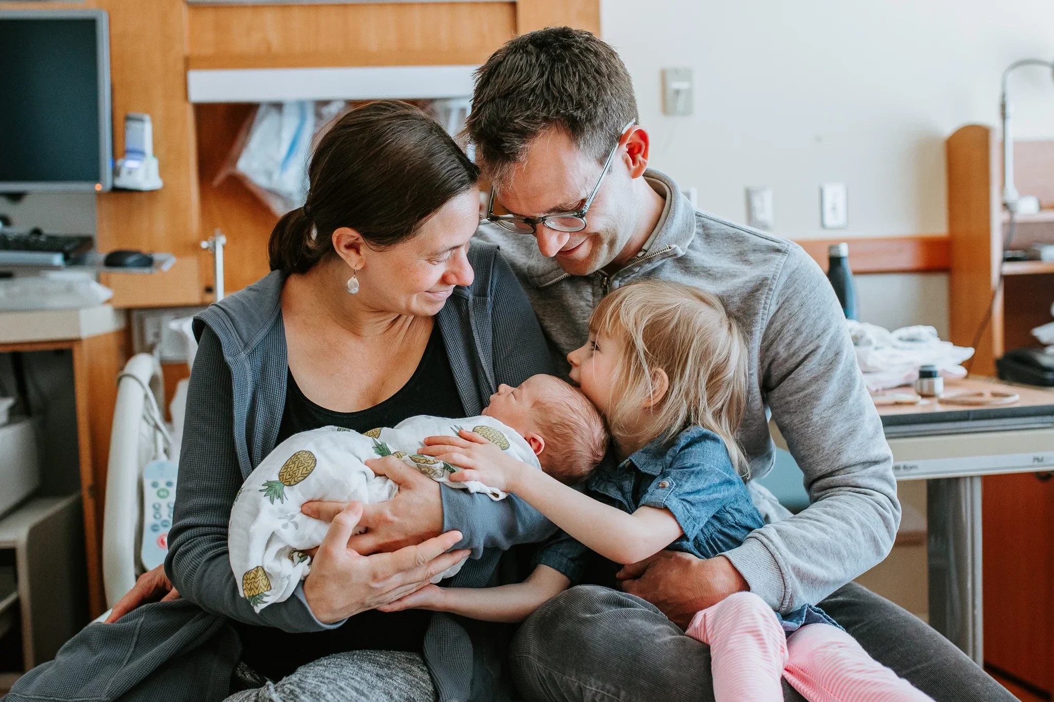 Two adults and a child admire a baby in a hospital room